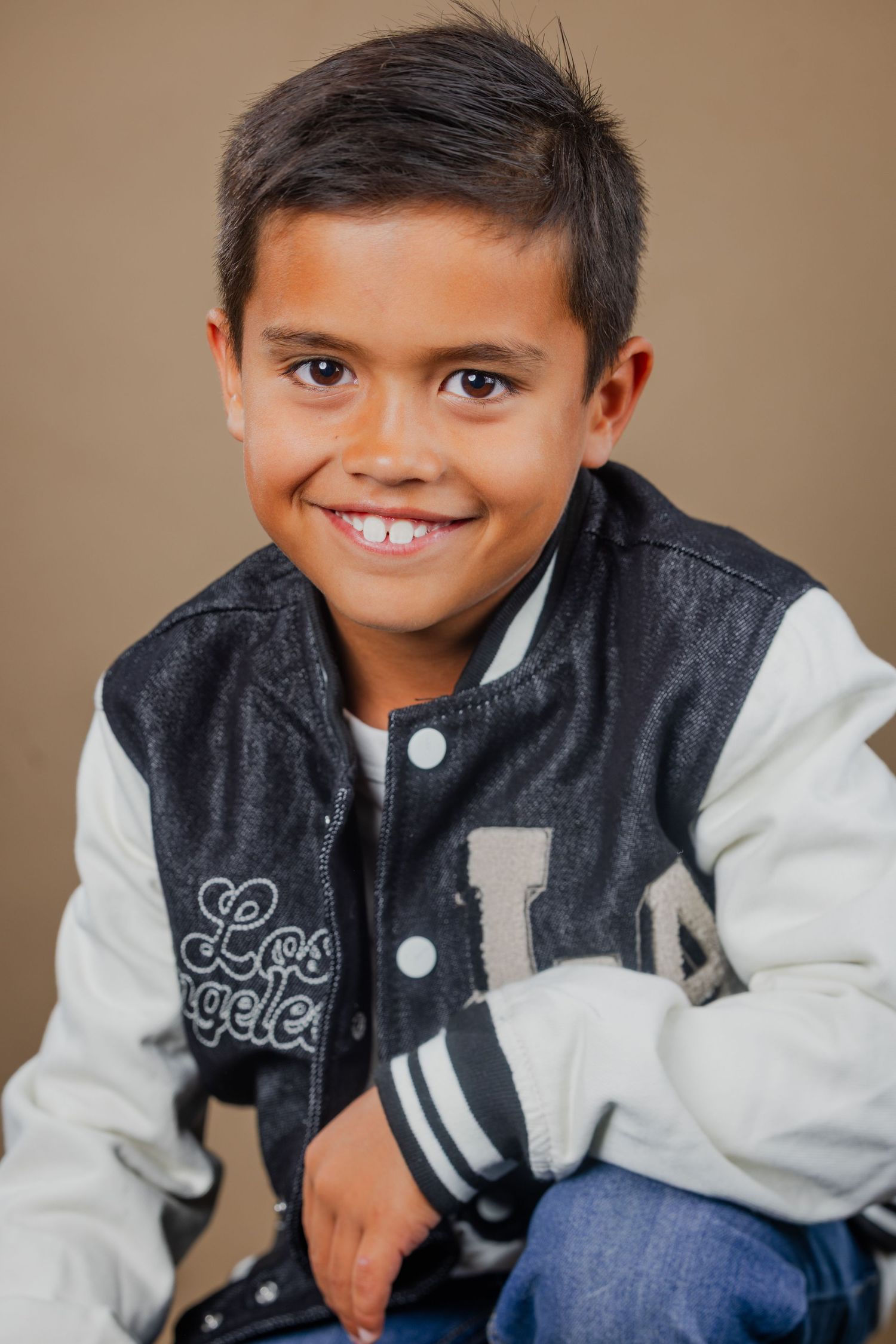 Smiling young Latino boy in a Los Angeles varsity jacket posing for a studio portrait.
