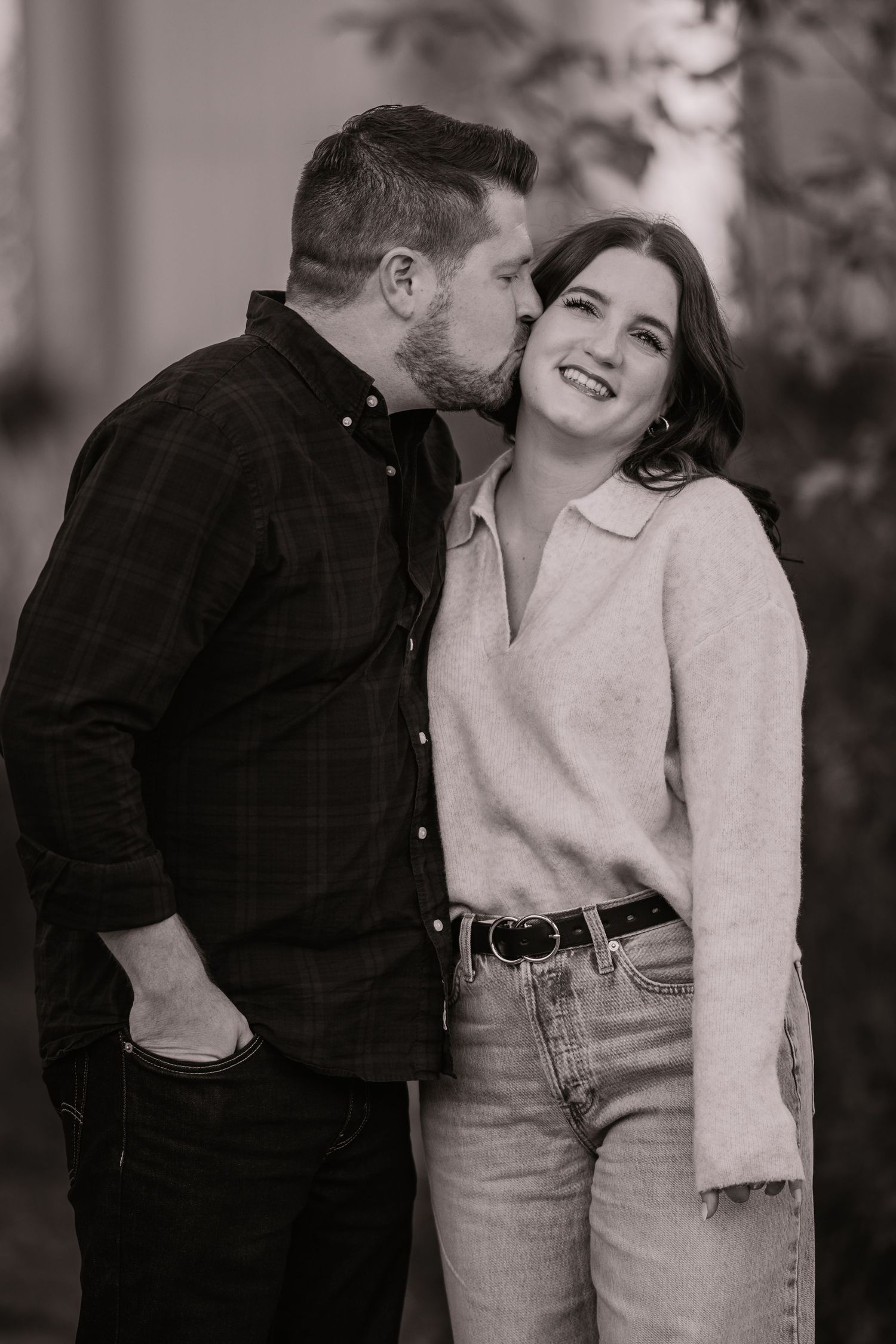 Black and white photo of couple, man kissing woman on cheek outdoors.