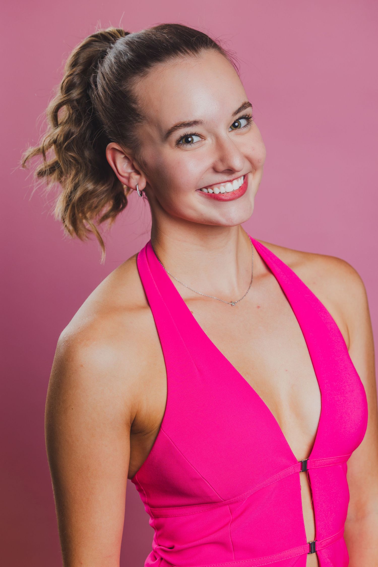 Smiling woman in hot pink halter dress with ponytail poses against matching pink background.