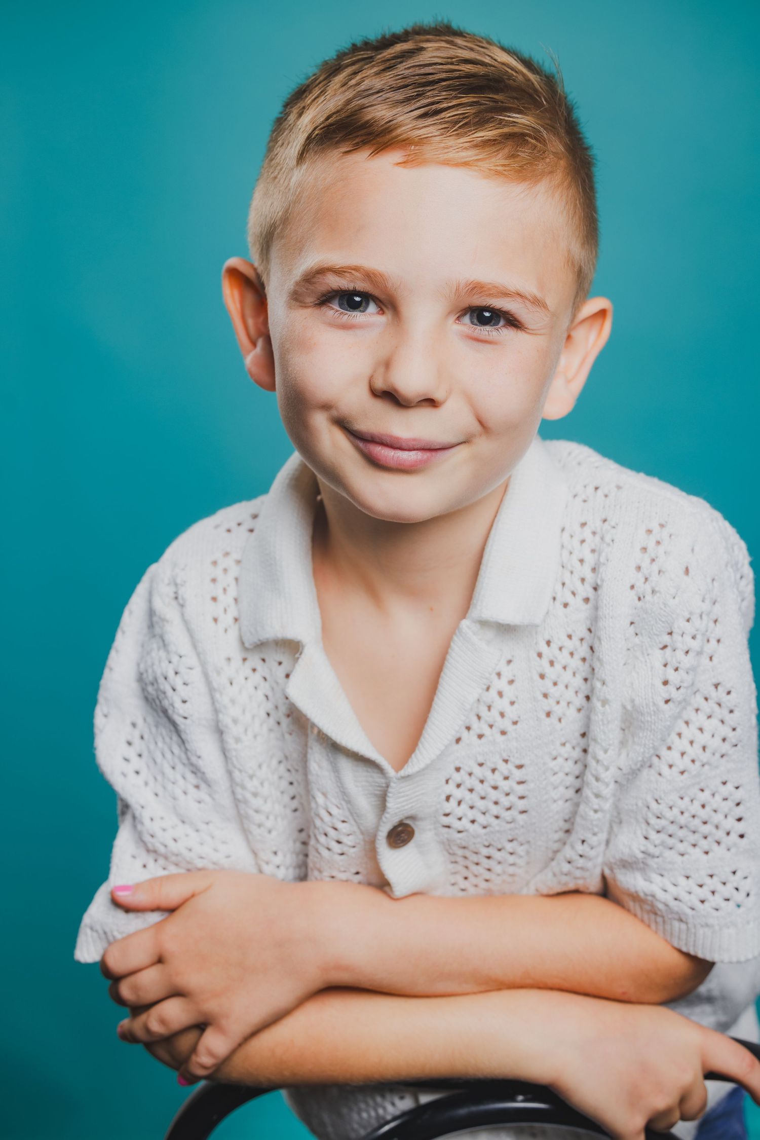 Smiling young boy in white knit shirt posing against blue background.