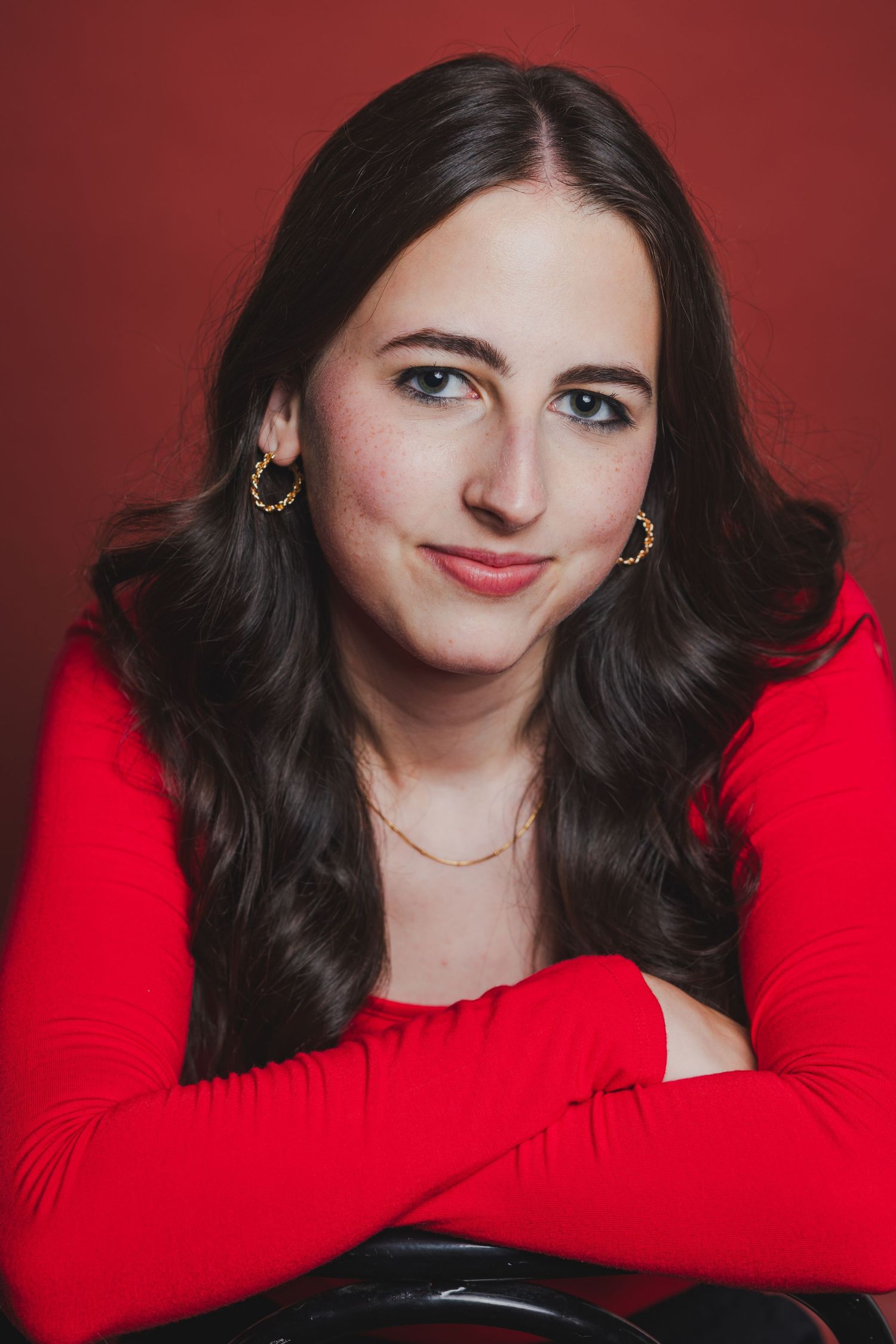 Young woman with dark wavy hair in a red top posing against a red background.