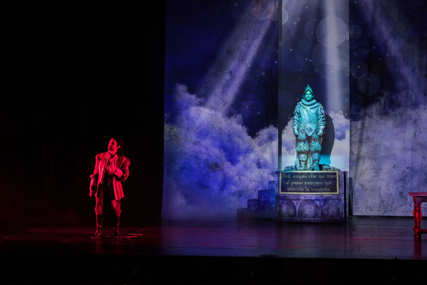 A dramatic stage scene features a red-lit performer beside a glowing blue deity statue with fog effects.
