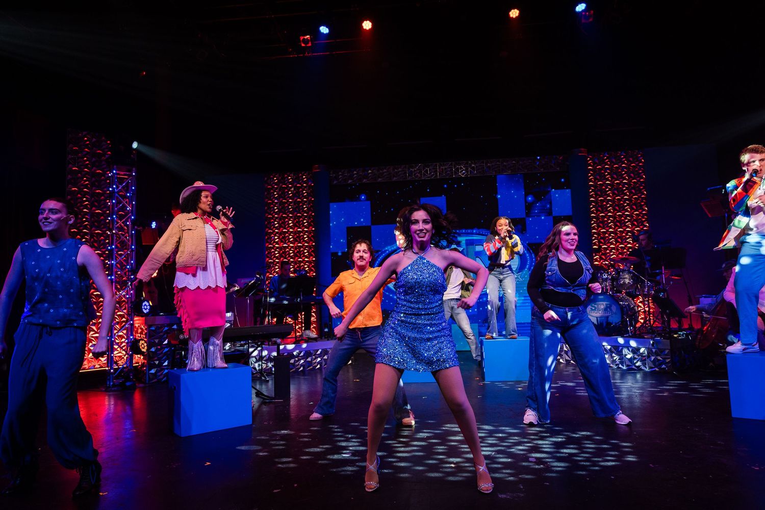Colorful theatrical performance with dancers on stage under vibrant blue and orange lights.