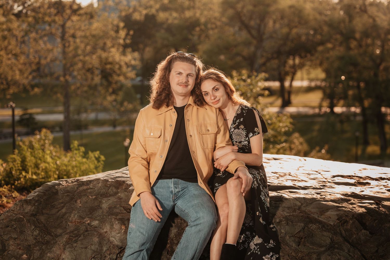 Happy couple sits closely together on a large rock in a scenic autumn park.