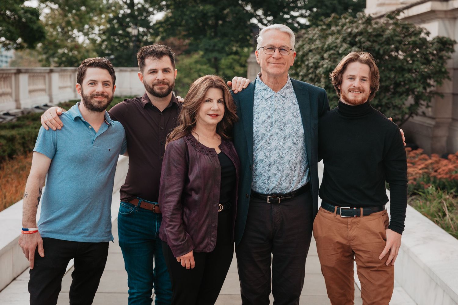 A family of five adults smiles together outdoors in a warm, candid group portrait.