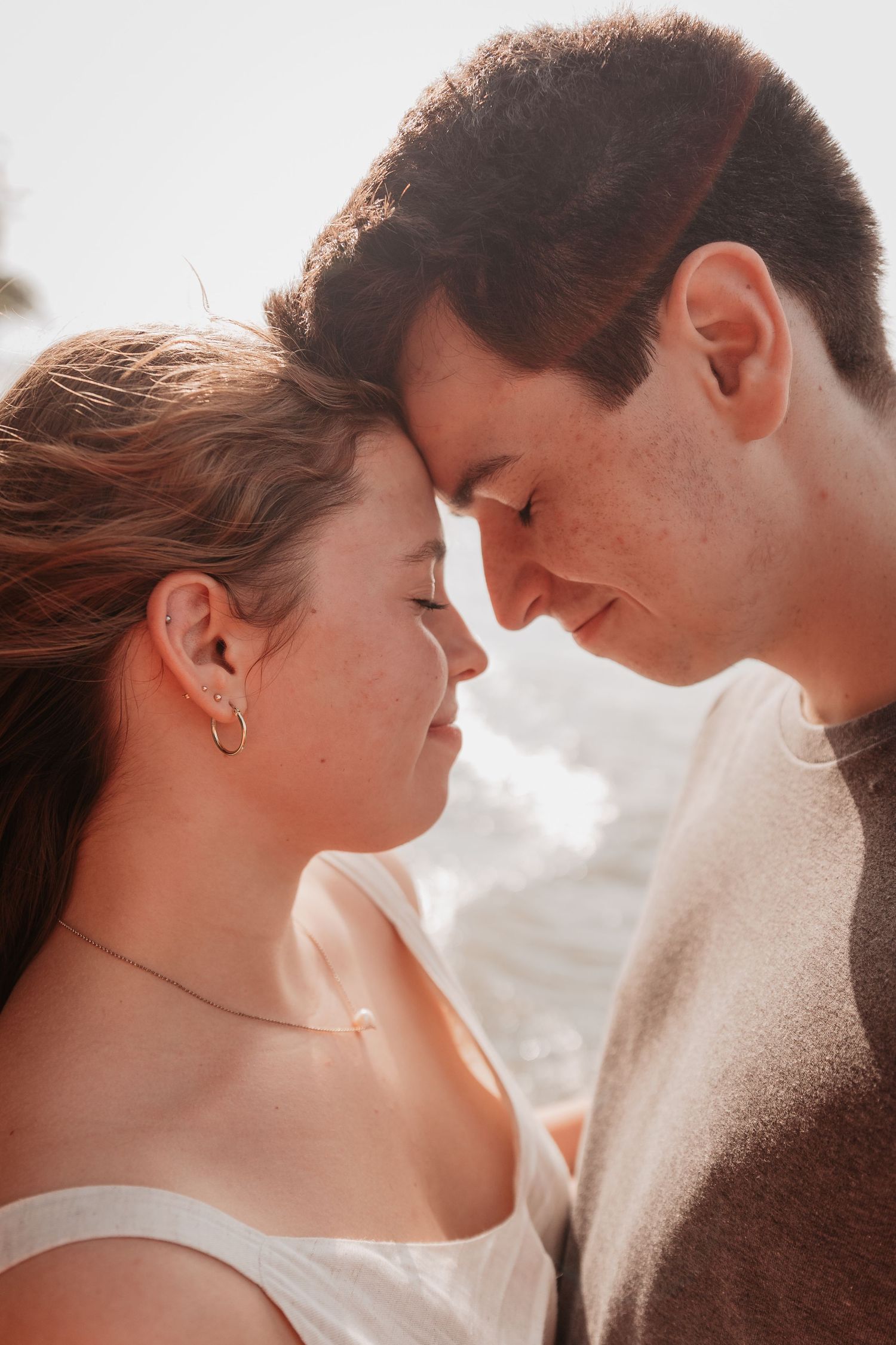 A romantic couple touches foreheads tenderly in a soft, sun-kissed close-up portrait.