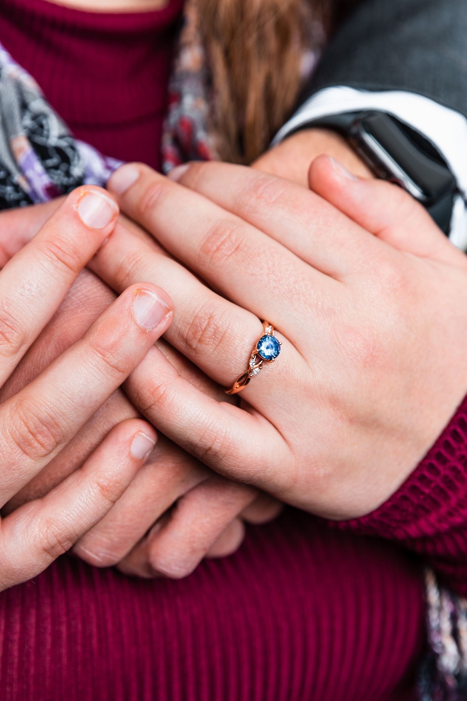 Close-up of couple's hands showing a beautiful blue sapphire engagement ring in rose gold.