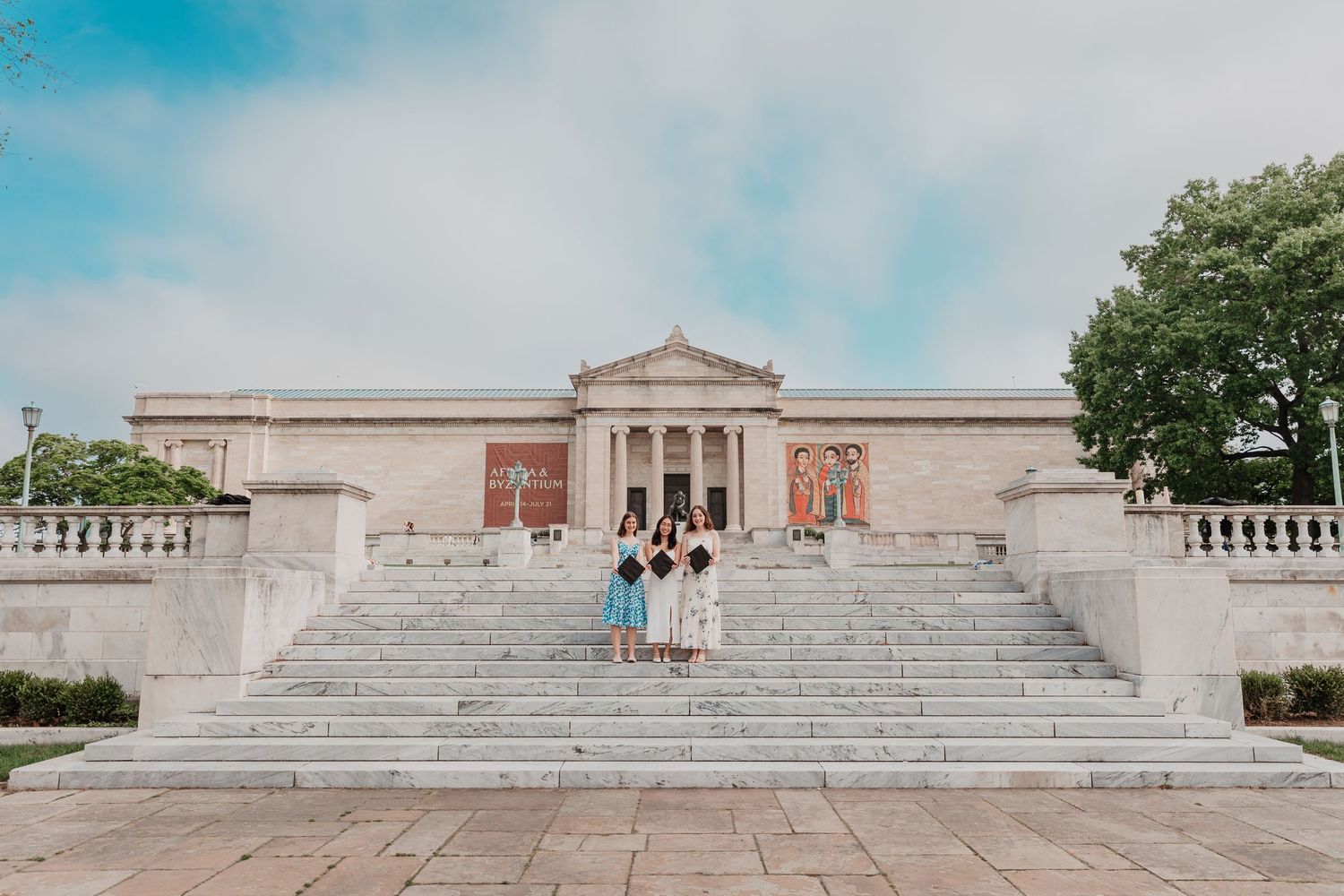 Group of graduates posing on grand steps of a neoclassical museum building outdoors.