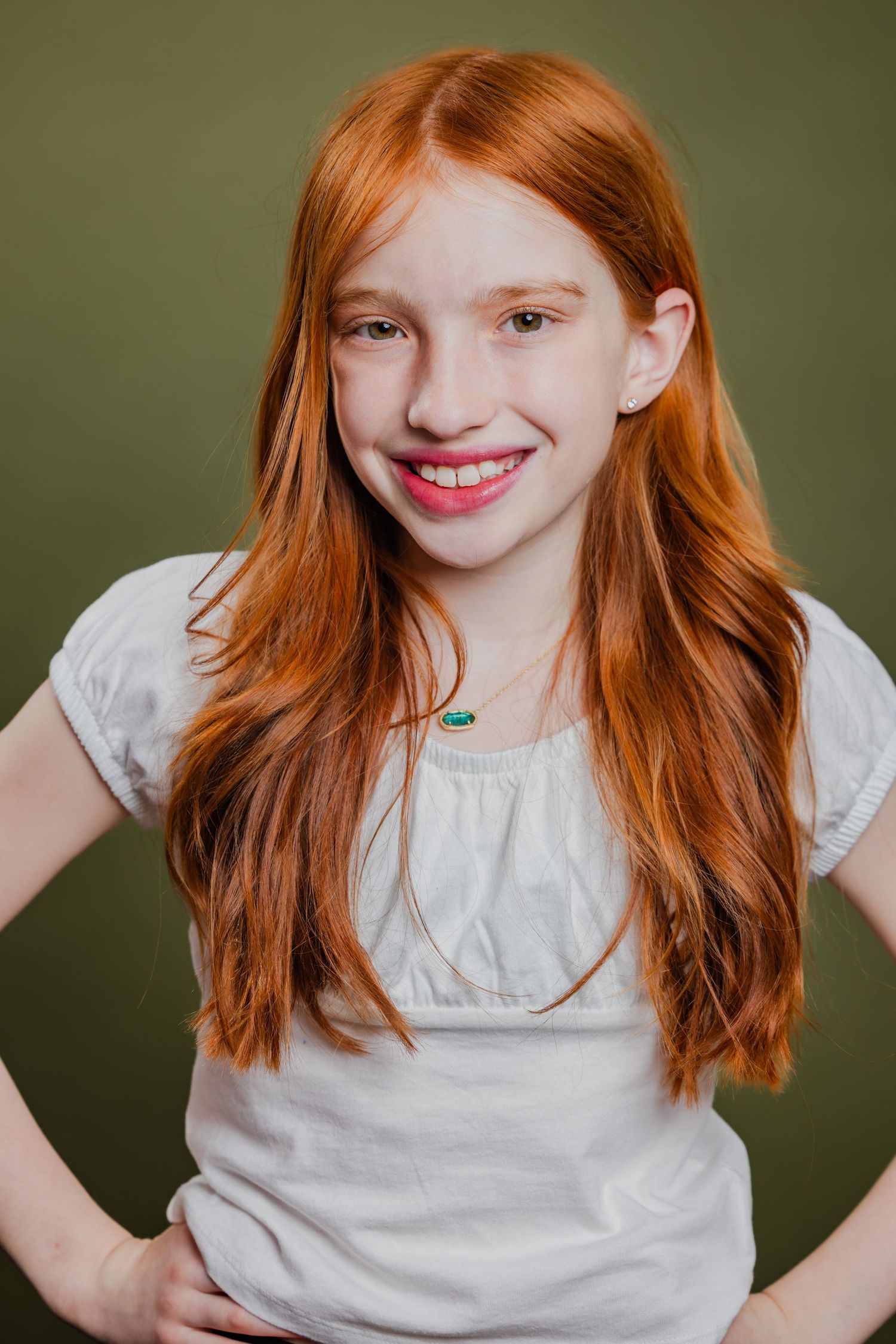Redhead girl with long hair in a white top smiling confidently against an olive green background.