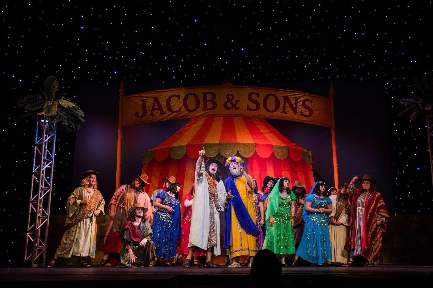 Cast performs under a Jacob and Sons circus tent sign in a vibrant biblical musical.