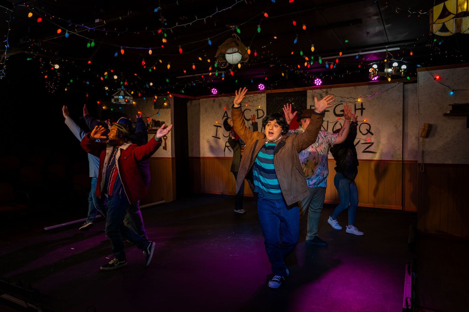 Ensemble cast dancing on stage under colorful lights during a Stranger Things-inspired theatrical production.