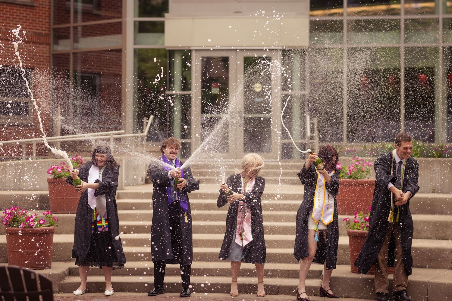 Group of graduates celebrating by spraying champagne outside university building.