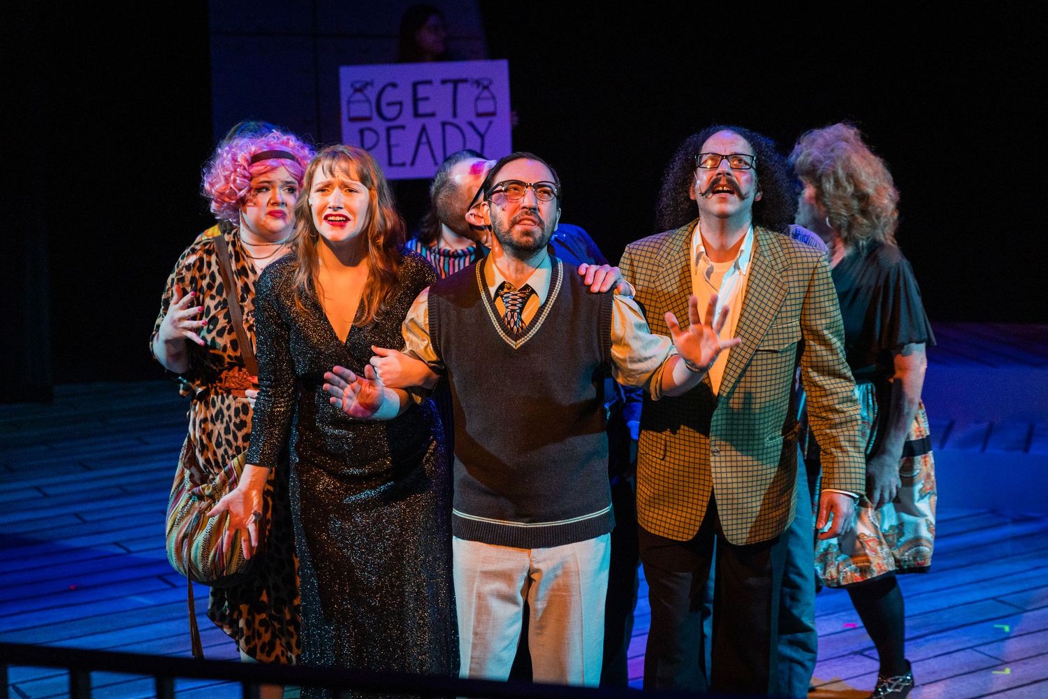 Five theater cast members posing together on stage holding a Get Ready sign.