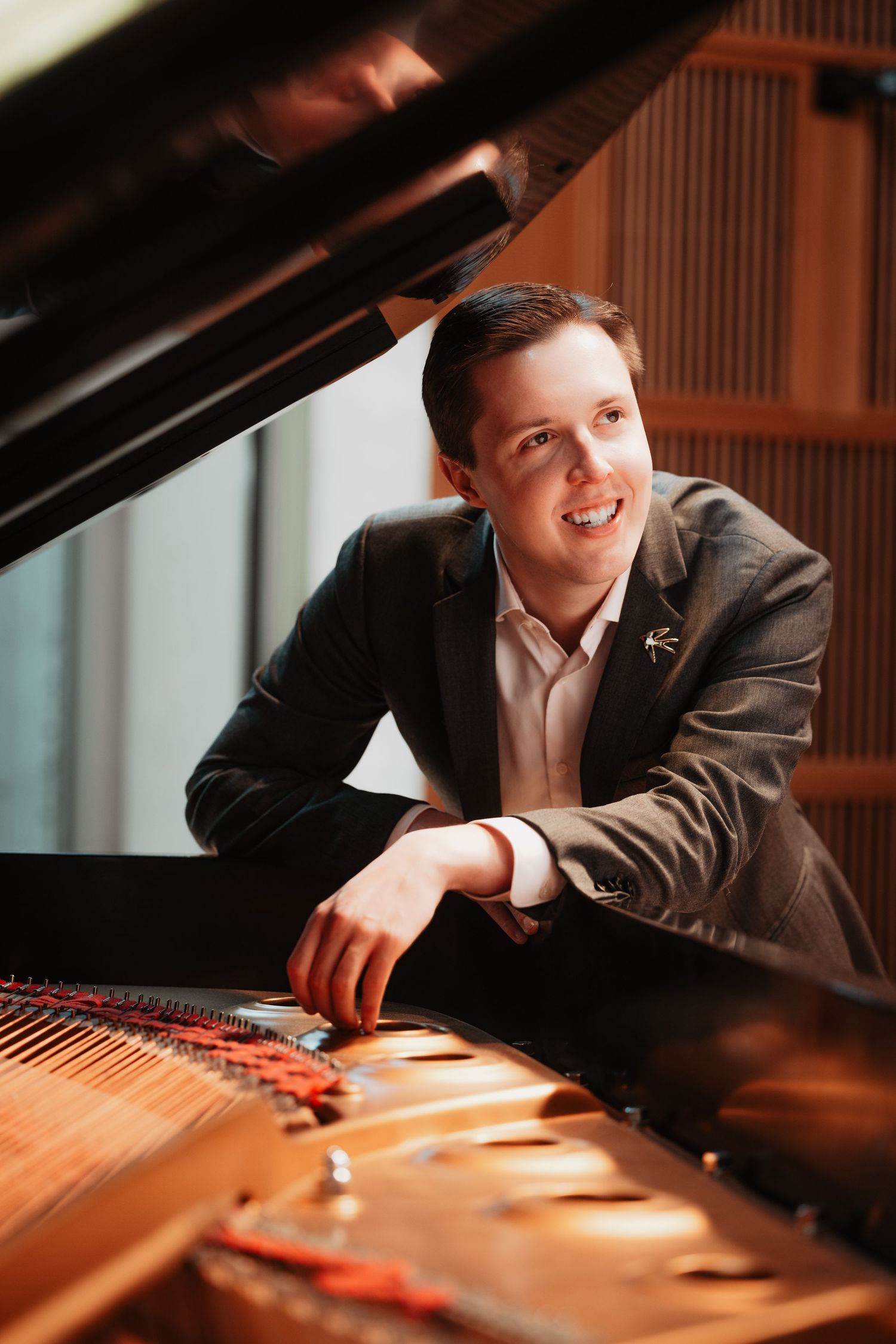 Smiling young man in blazer leaning on grand piano keys.