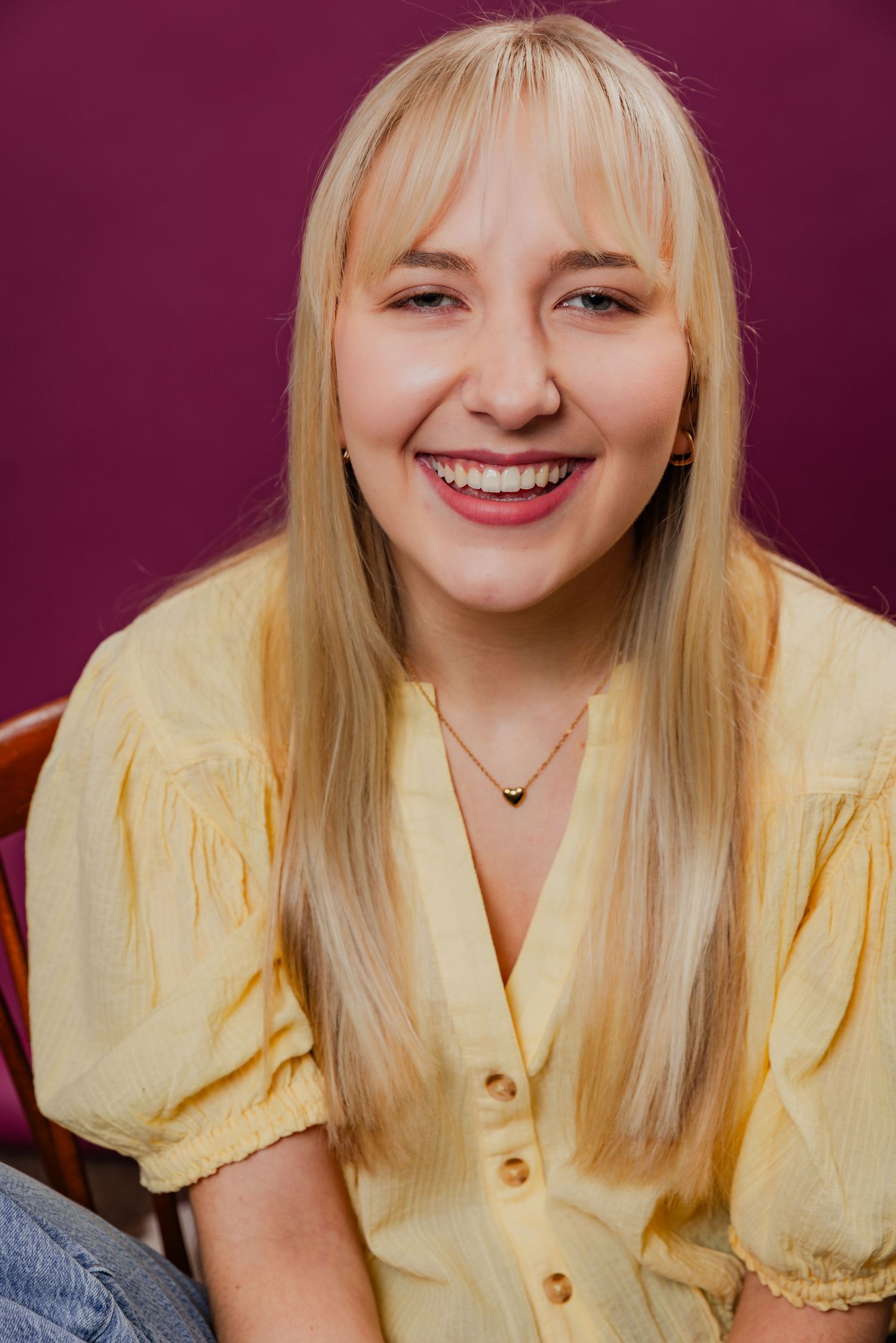 Smiling blonde woman with bangs wearing yellow blouse, cheerful studio portrait photo.