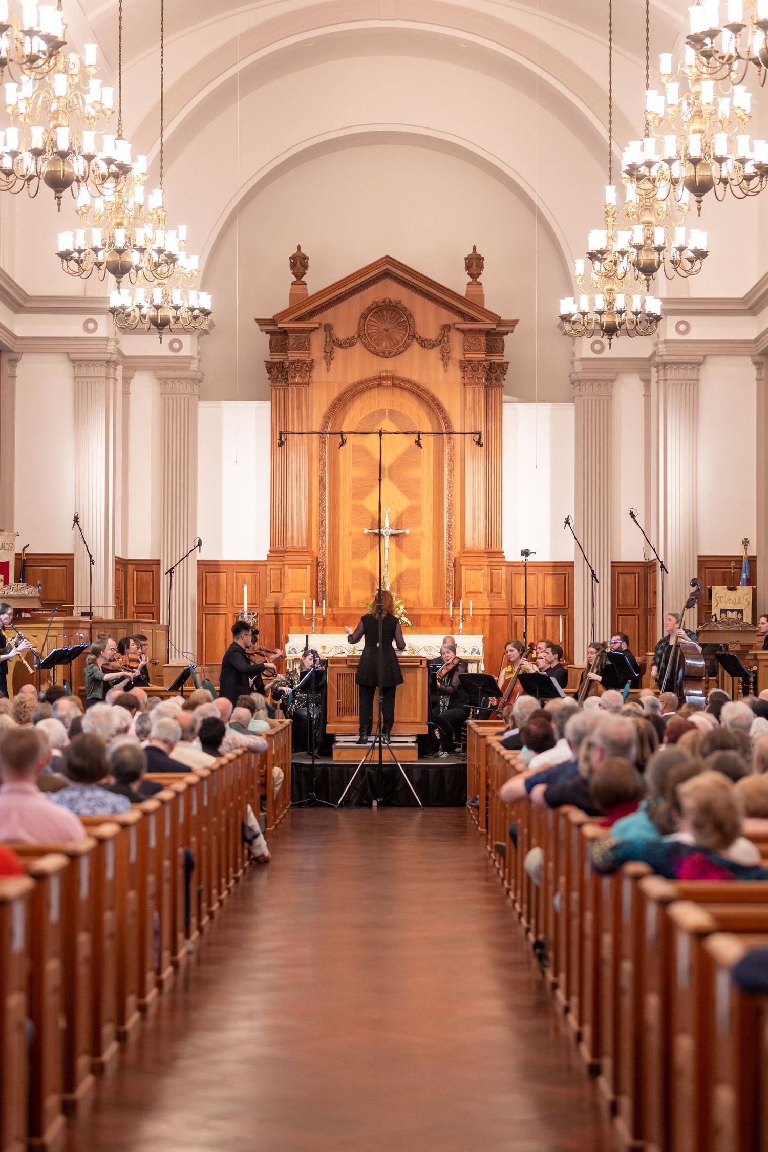 A conductor leads a chamber orchestra before a wooden altar in a classical church setting.