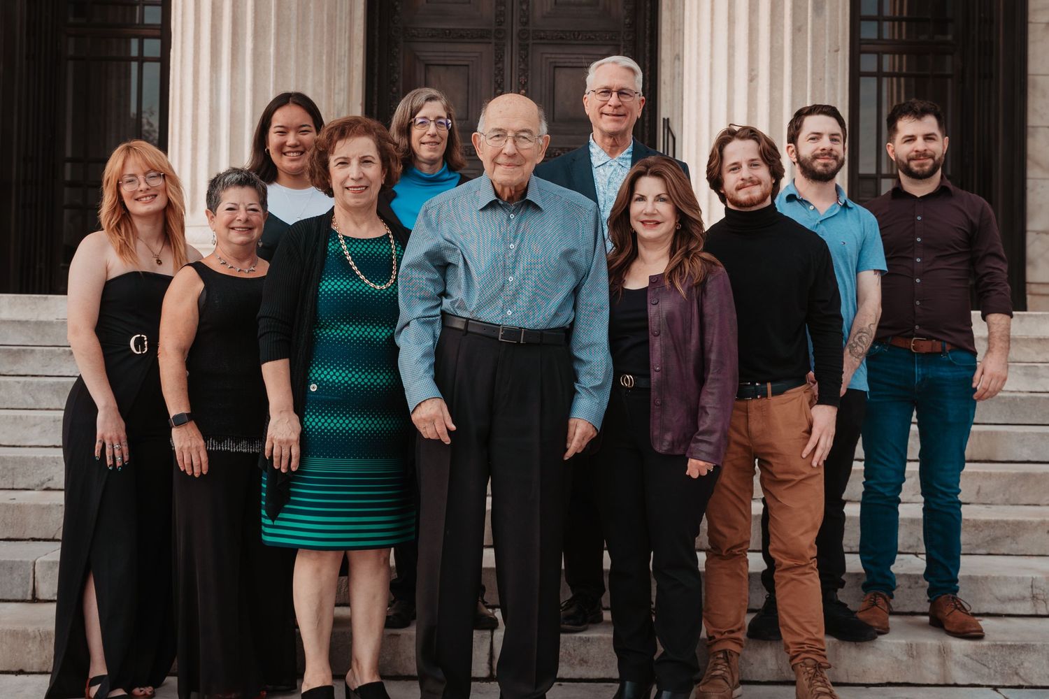 Large family group portrait on stone steps, smiling together in coordinated teal and black outfits.