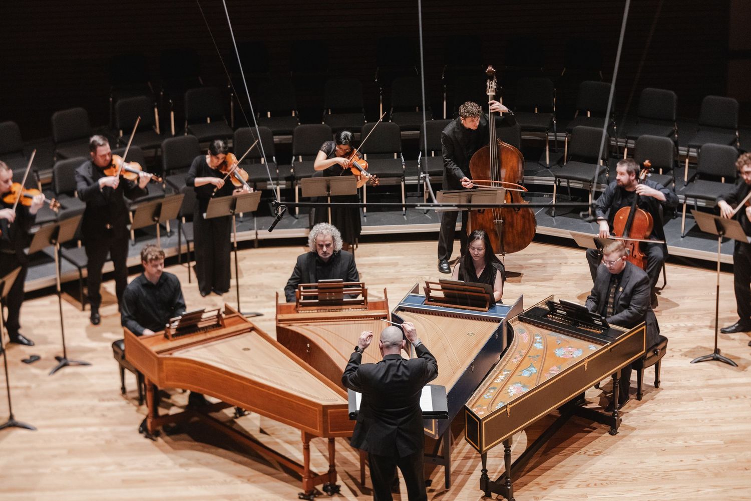 Chamber orchestra performing in a concert hall with harpsichords arranged in a circle.