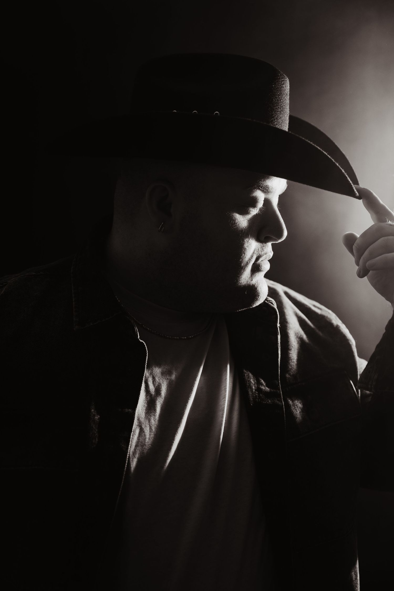 Dramatic black and white portrait of a man in a cowboy hat touching its brim.