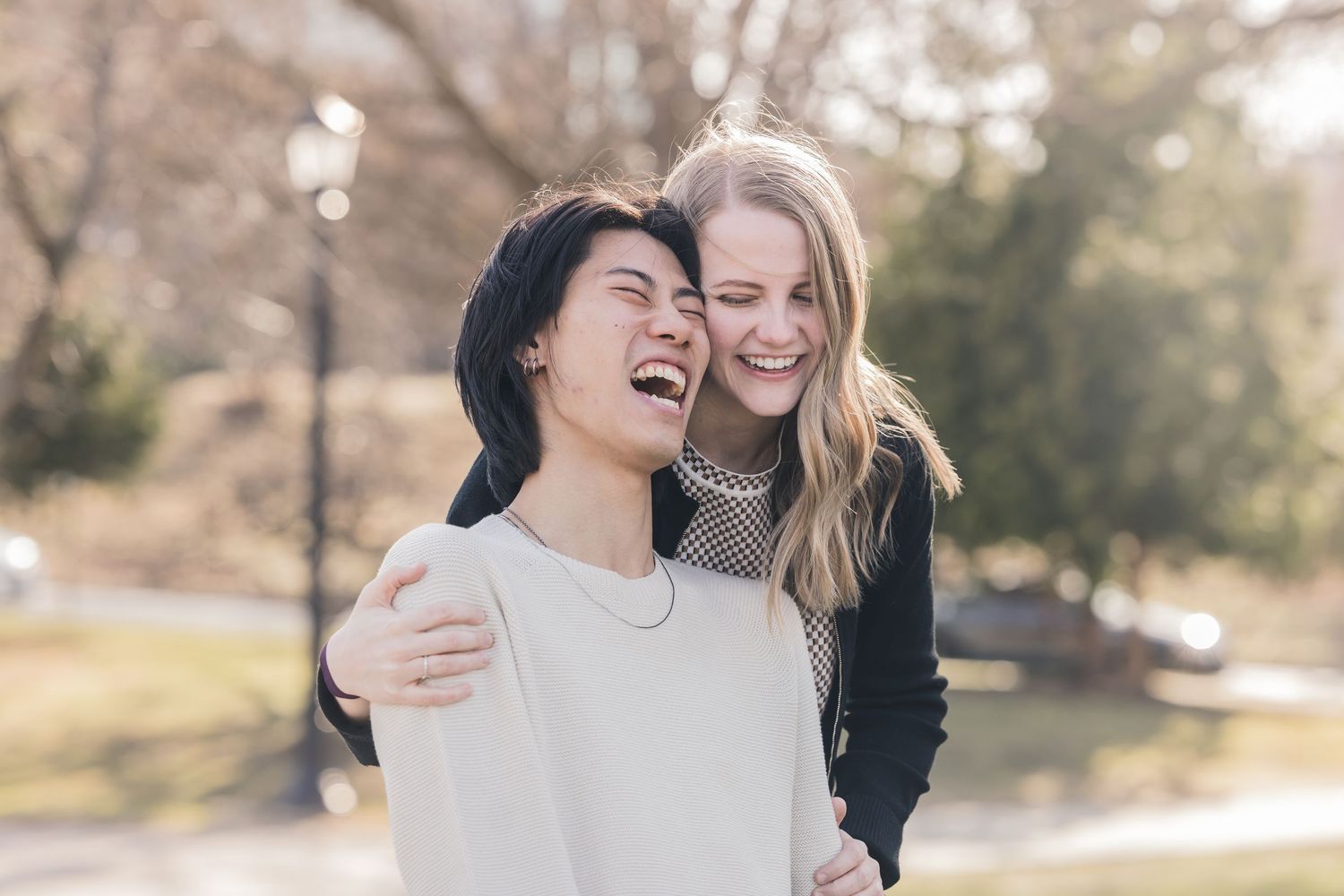 Joyful young couple laughing and embracing outdoors in a sunny park setting.