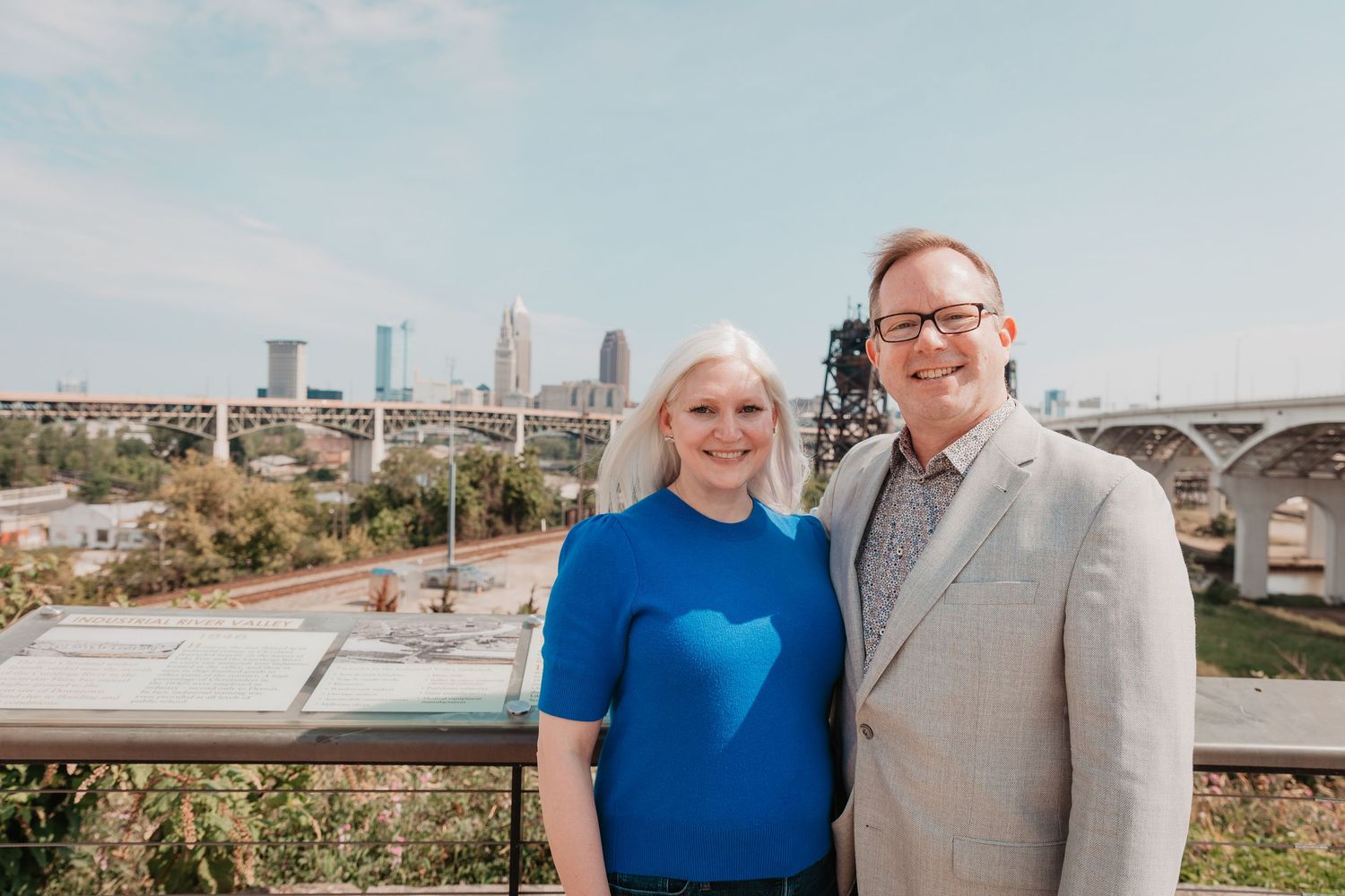 A smiling couple poses together with the Cleveland city skyline in the background.