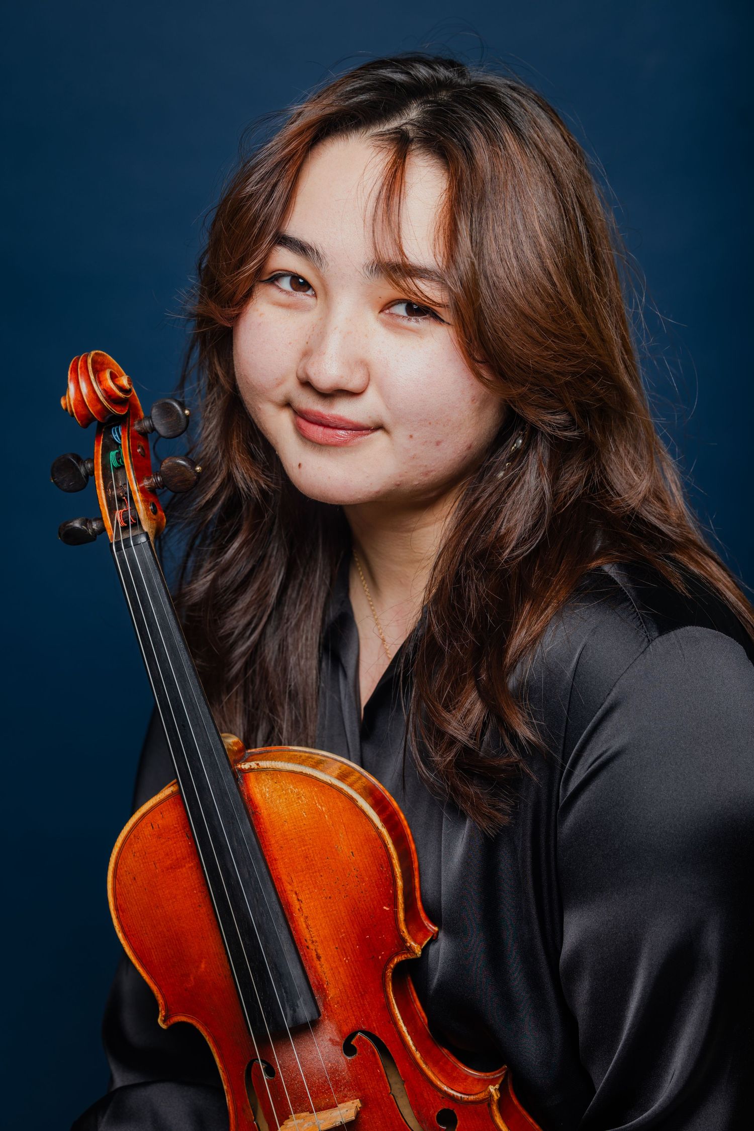 Young woman with long hair holding a violin against a dark blue background.