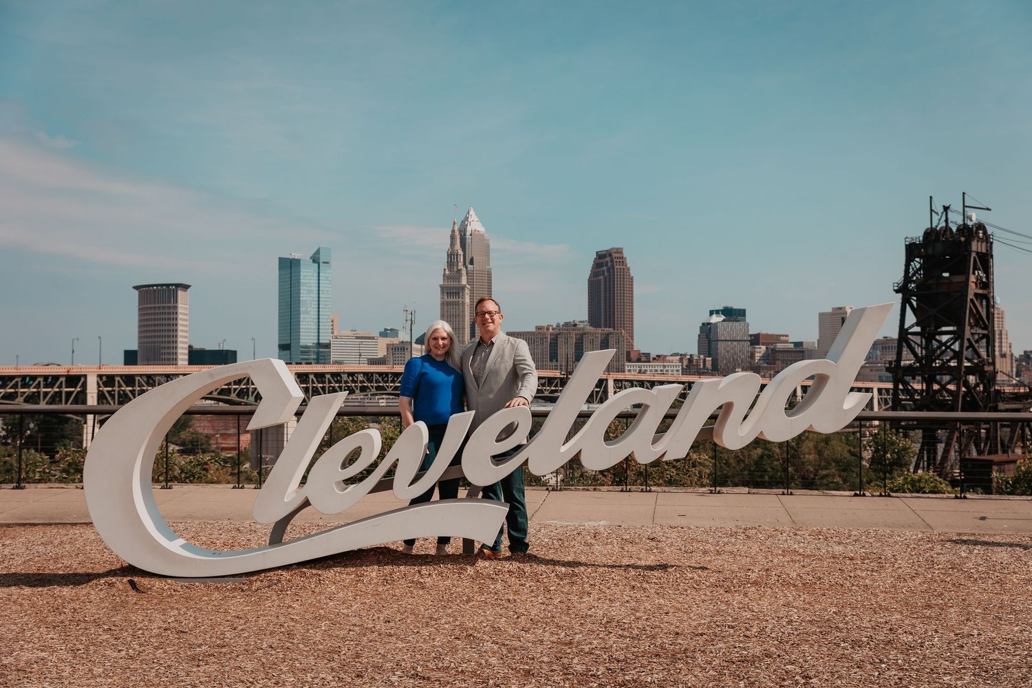 A couple stands in front of a large Cleveland script sign with the city skyline behind them.
