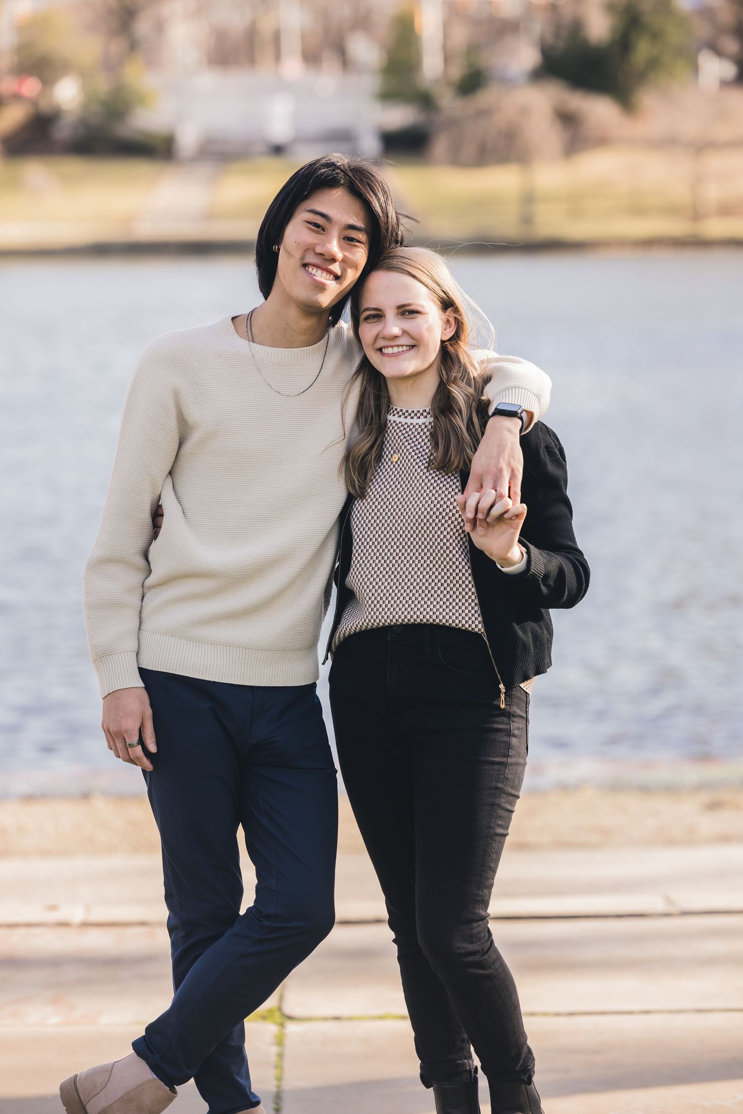 Young couple smiling arm in arm beside a serene lake on a clear day.