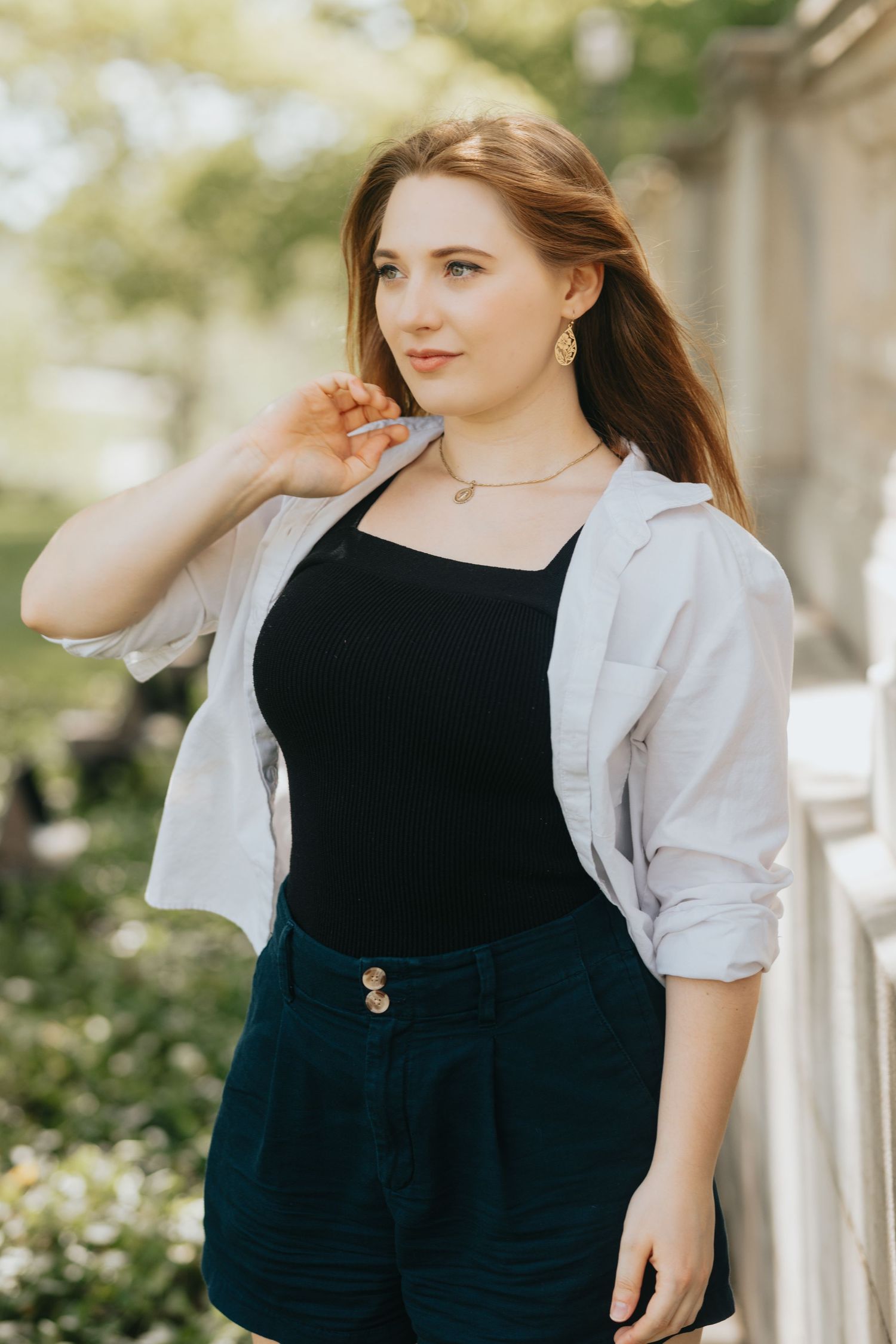Young woman in white shirt and black top posing outdoors in natural sunlight.