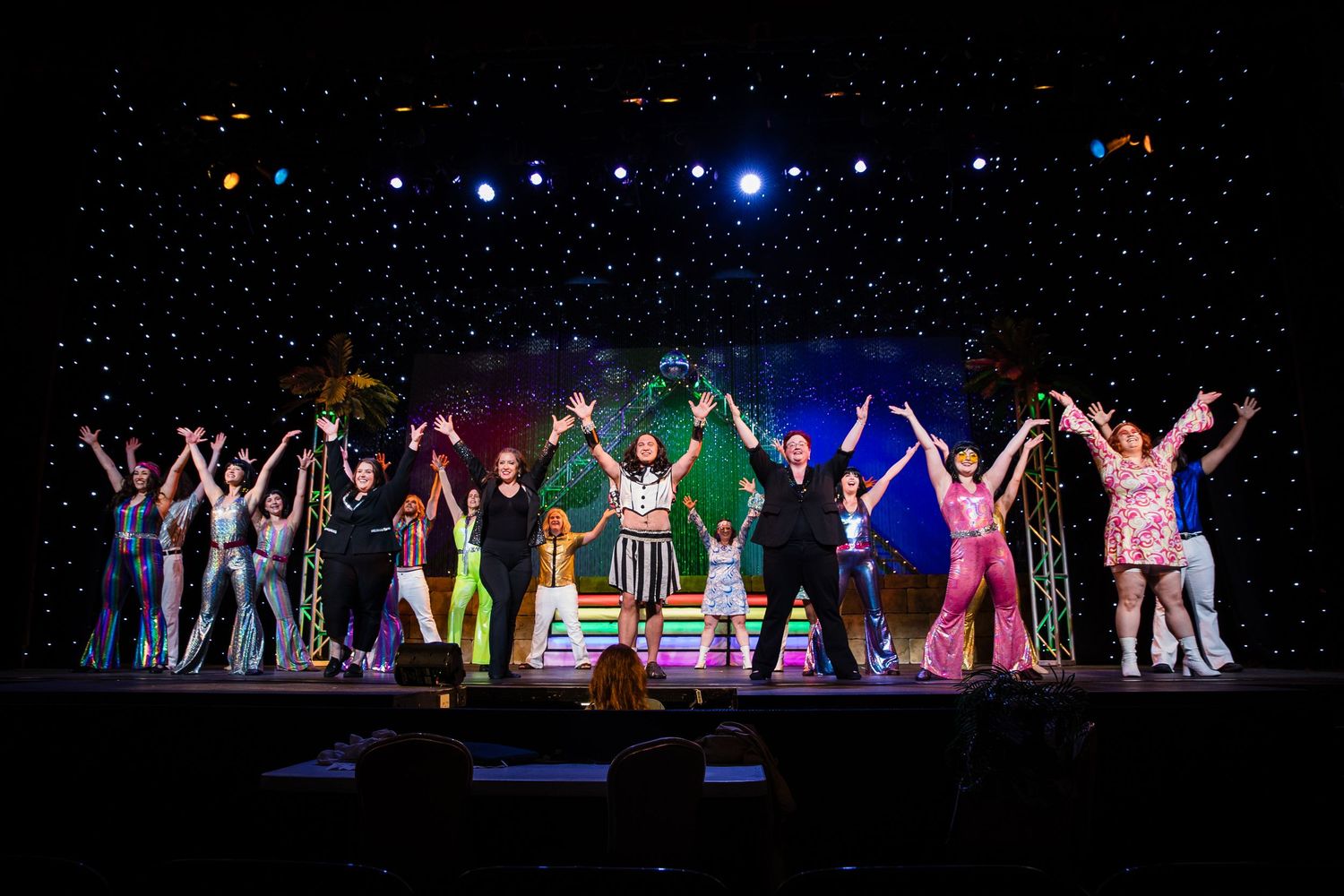Full cast of a colorful musical theater production takes a bow on a star-lit stage.