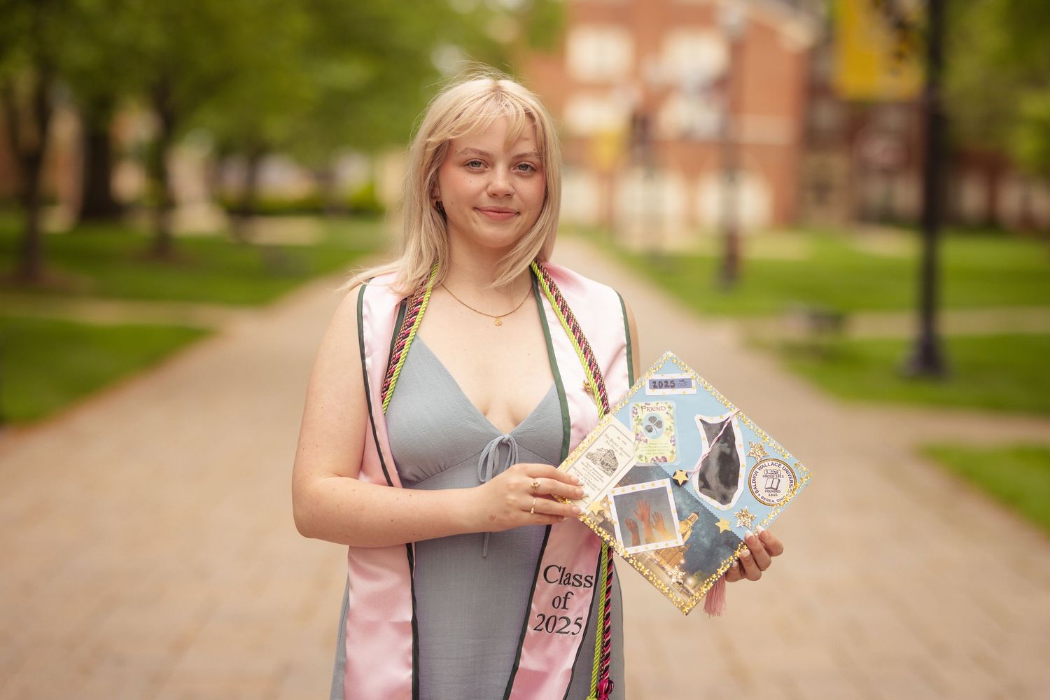 Smiling blonde female graduate holding photo collage wearing Class of 2023 graduation sash.