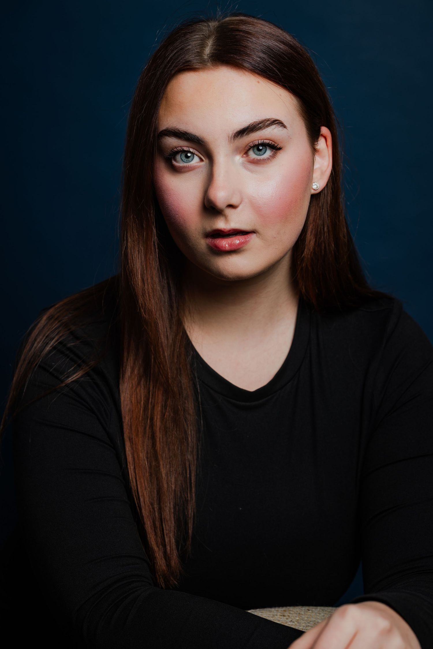 Young woman with long dark hair and blue eyes wearing a black top against a dark blue background.