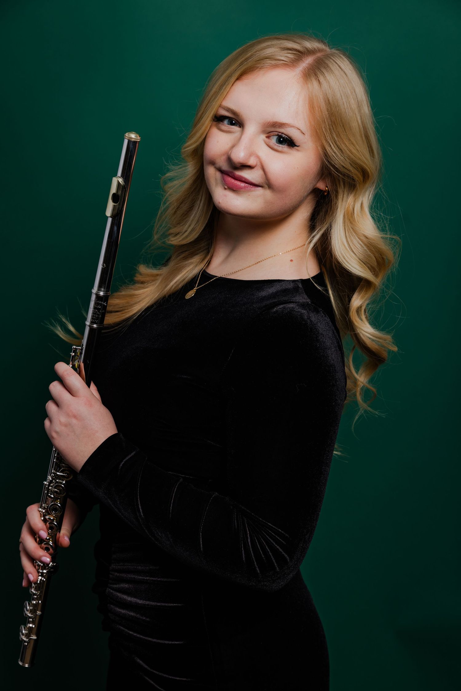 Blonde woman in black velvet dress holding a silver flute, green background portrait photo.
