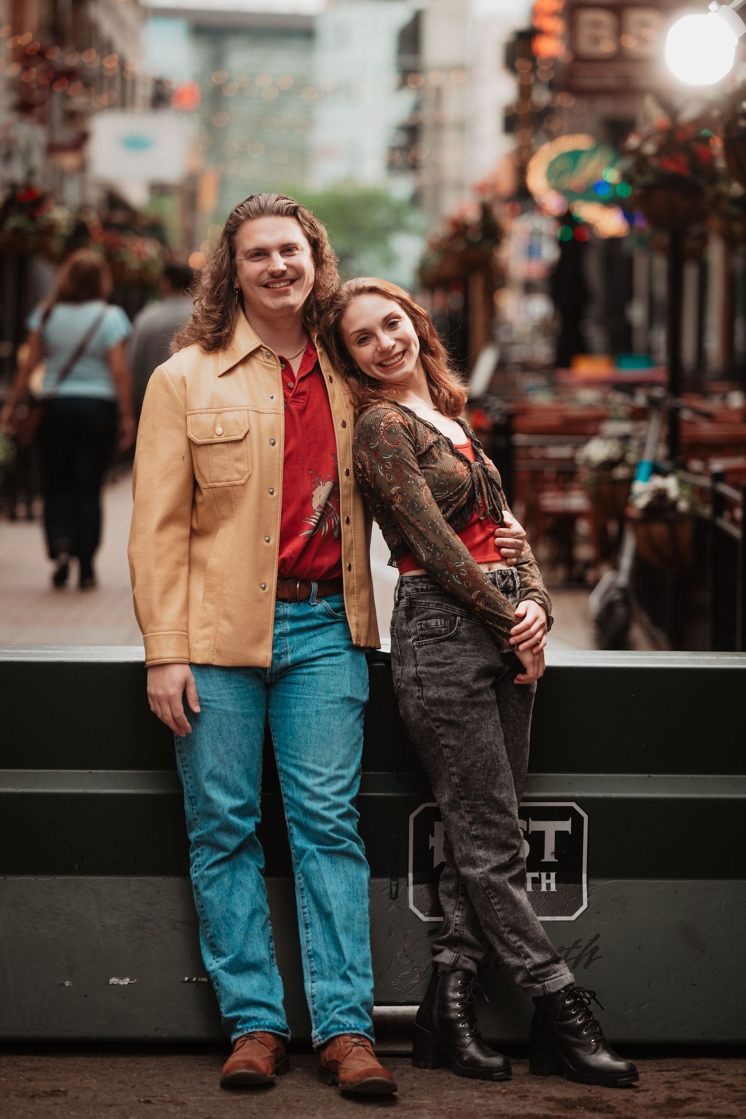 Smiling couple leans against a railing on a busy city street at dusk.