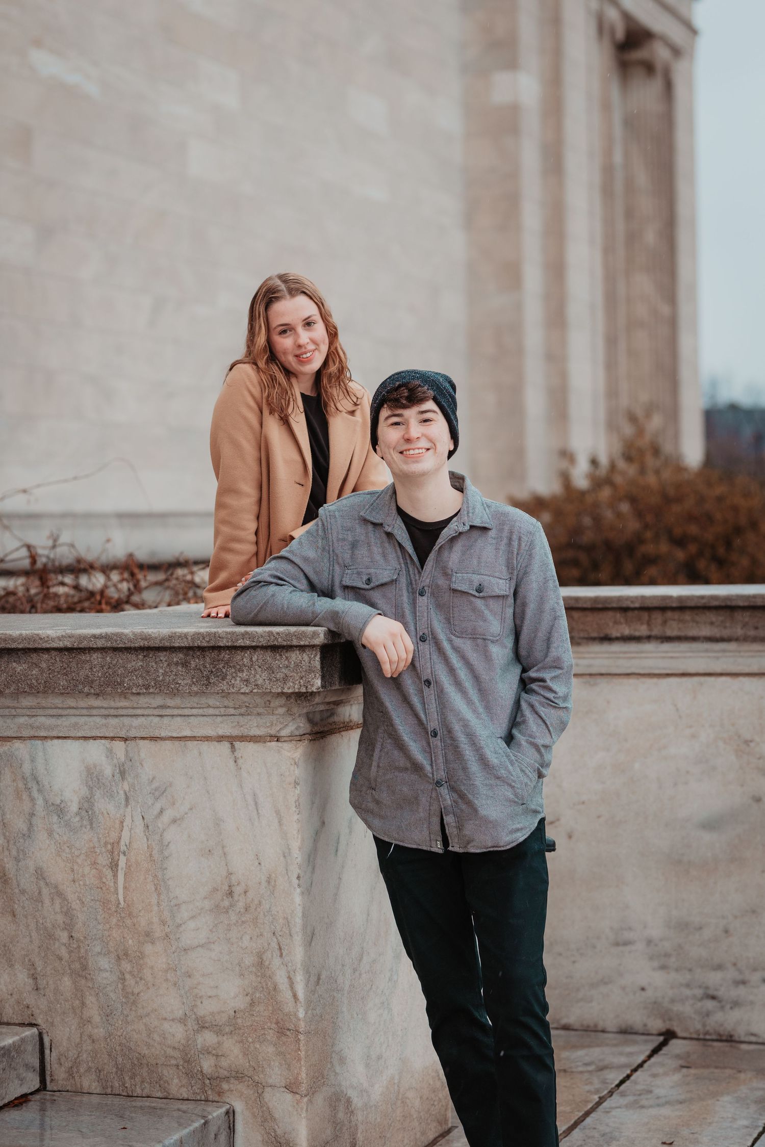 Young couple posing at stone monument, woman standing above man who leans casually on ledge.