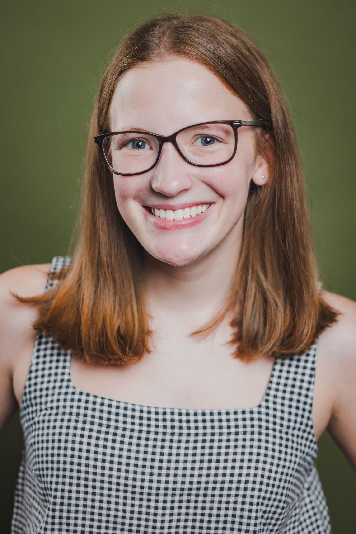 Smiling redhead young woman wearing glasses and checkered top against green background.