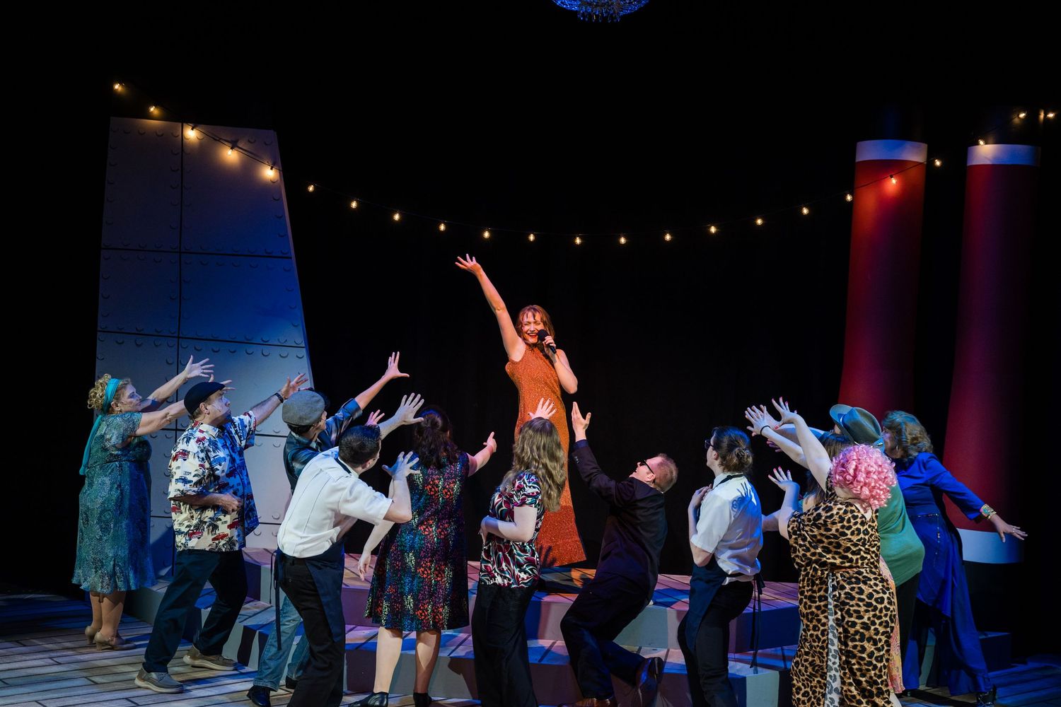 Theater cast lifting a central performer in a dramatic ensemble stage production scene.
