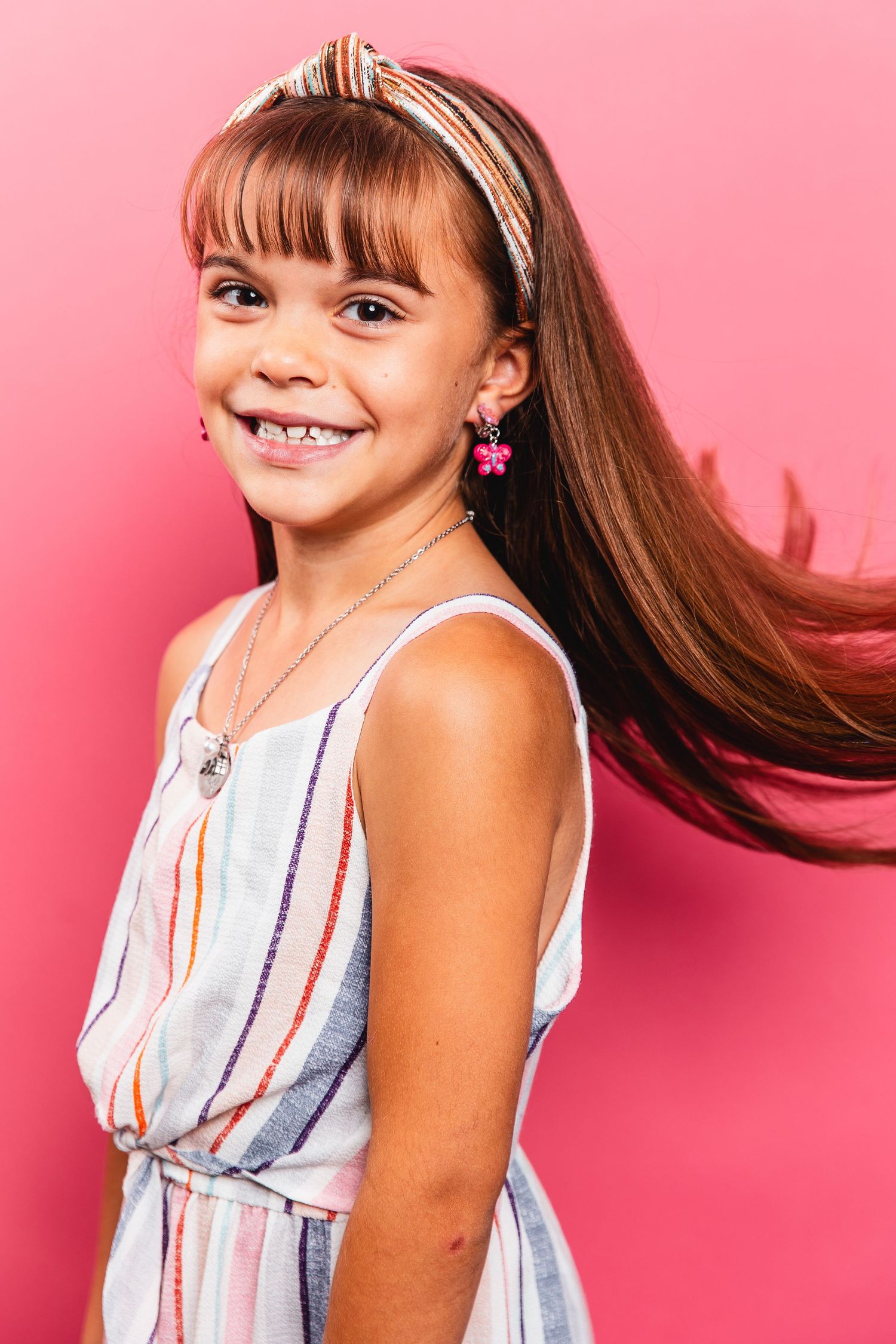 Happy young girl in striped dress with long flowing hair against pink background.