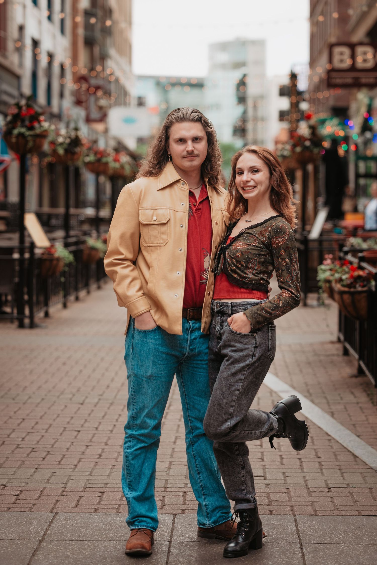Stylish couple poses together on a decorated urban street with city lights in background.