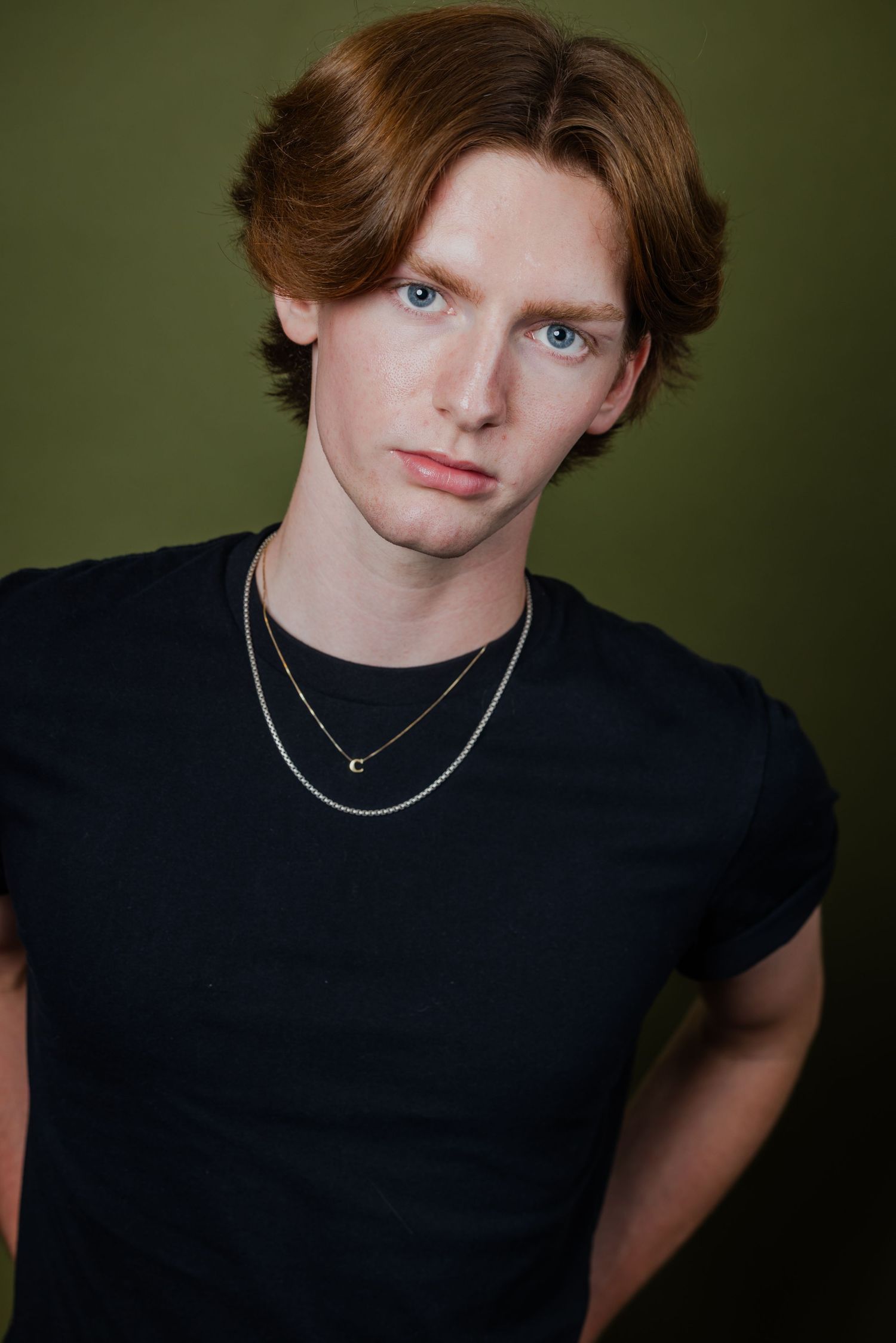Young man with auburn hair and blue eyes wearing a black t-shirt and layered necklaces.