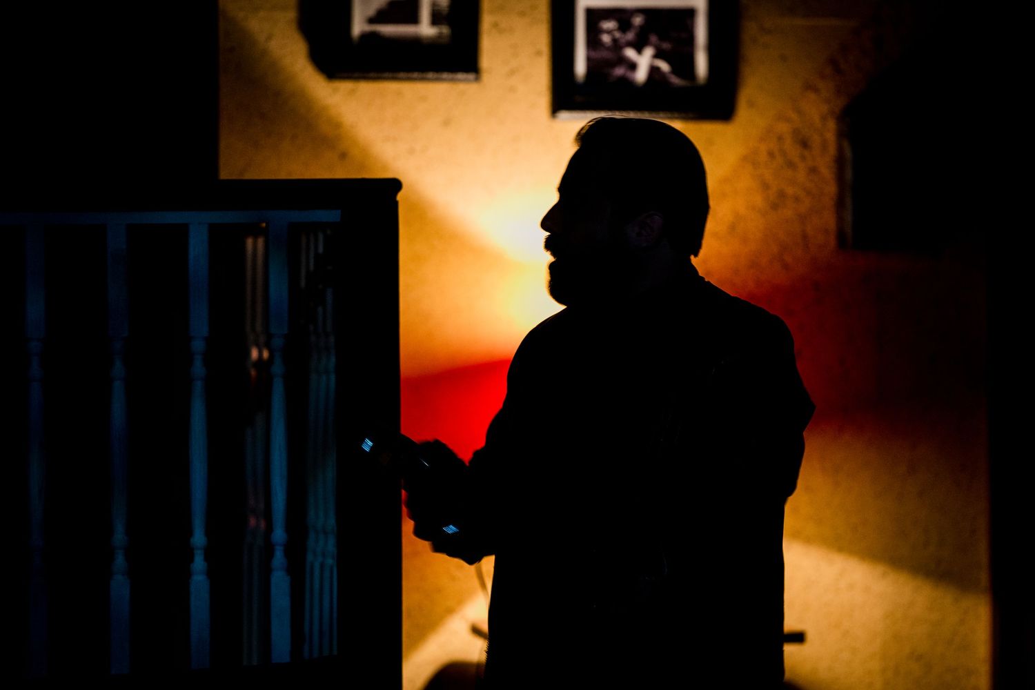 Dramatic silhouette of a man standing beside a cabinet bathed in warm amber stage lighting.