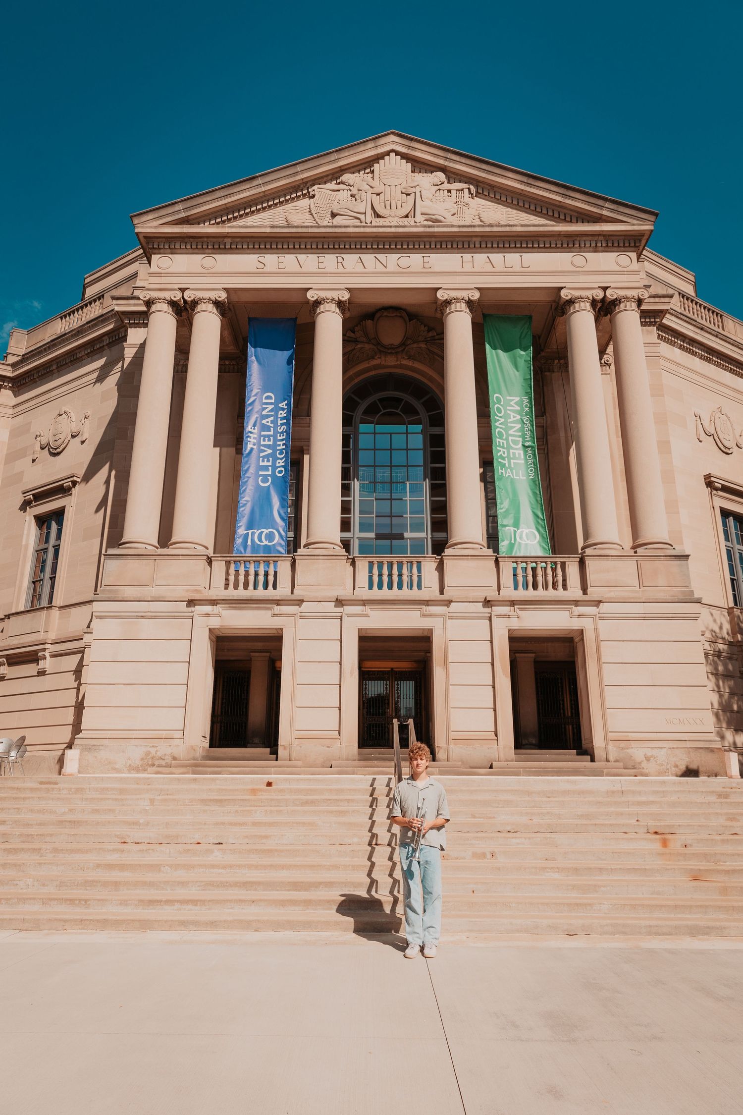 Woman standing at base of grand neoclassical building with Cleveland Orchestra banners on columns.