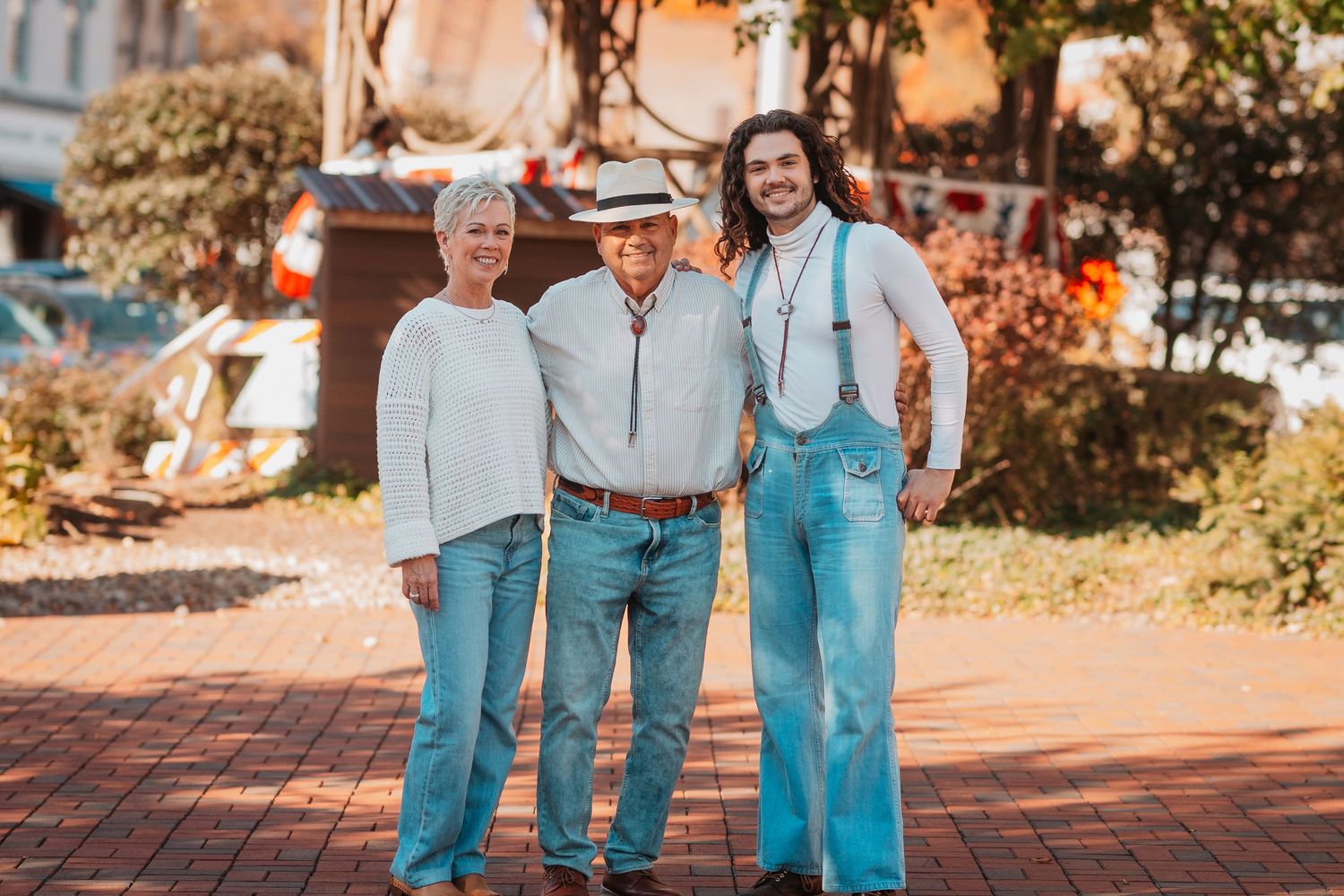 Three generations of family posing together on brick pathway in sunny outdoor setting.
