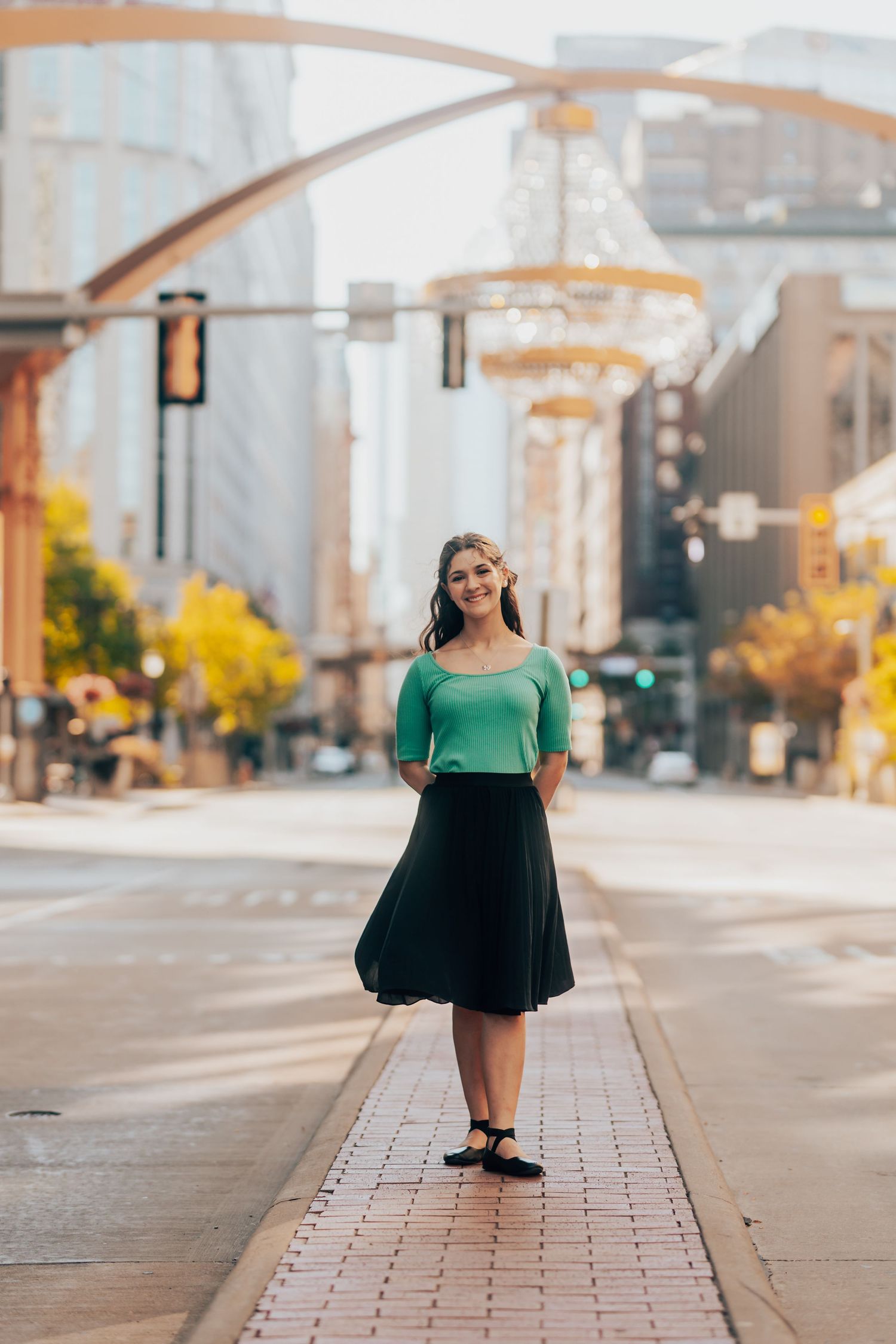 Woman in green top and black skirt standing on urban street.