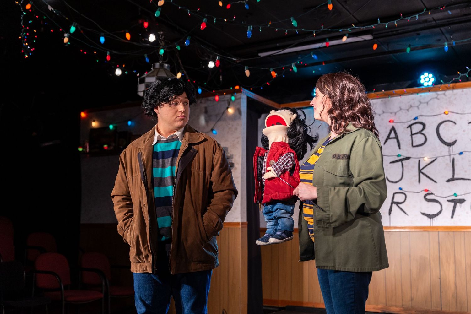 Two actors performing a Stranger Things-themed stage play with colorful lights and alphabet wall backdrop.