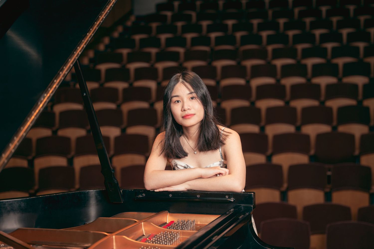Young woman resting on a grand piano in a warmly lit concert hall.