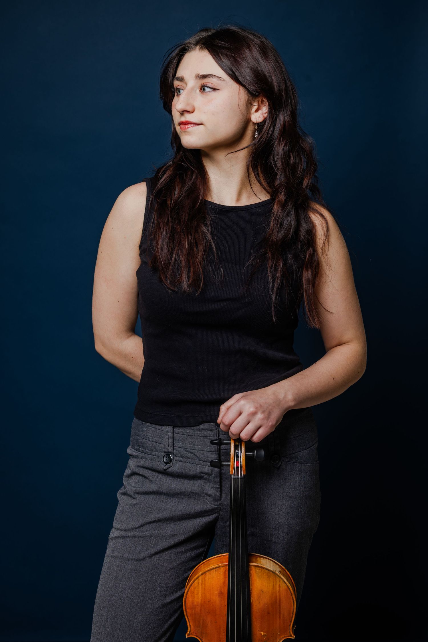 Young woman in black top holding a violin against a dark blue background.