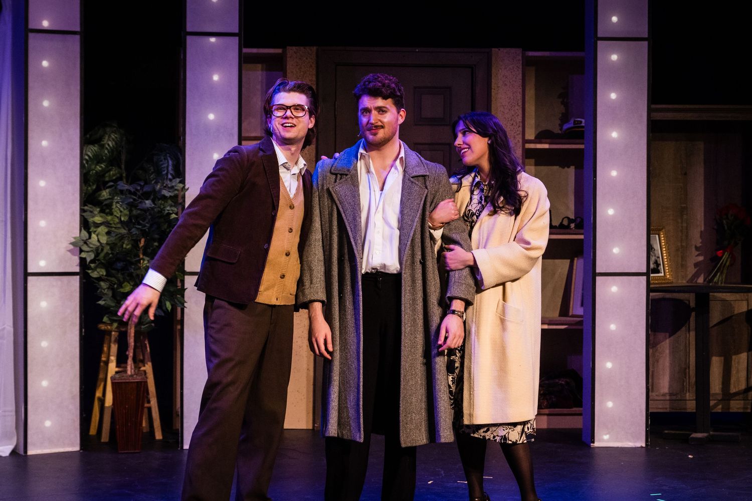 Three actors perform a dramatic scene on stage, two men and a woman in a theatrical production.