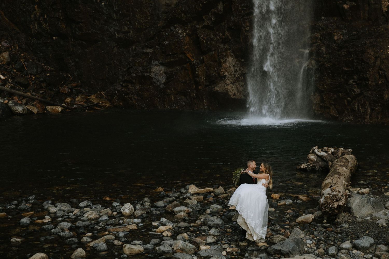 Couple embracing in front of a stunning waterfall on rocky shores during an outdoor elopement session near Seattle Washington