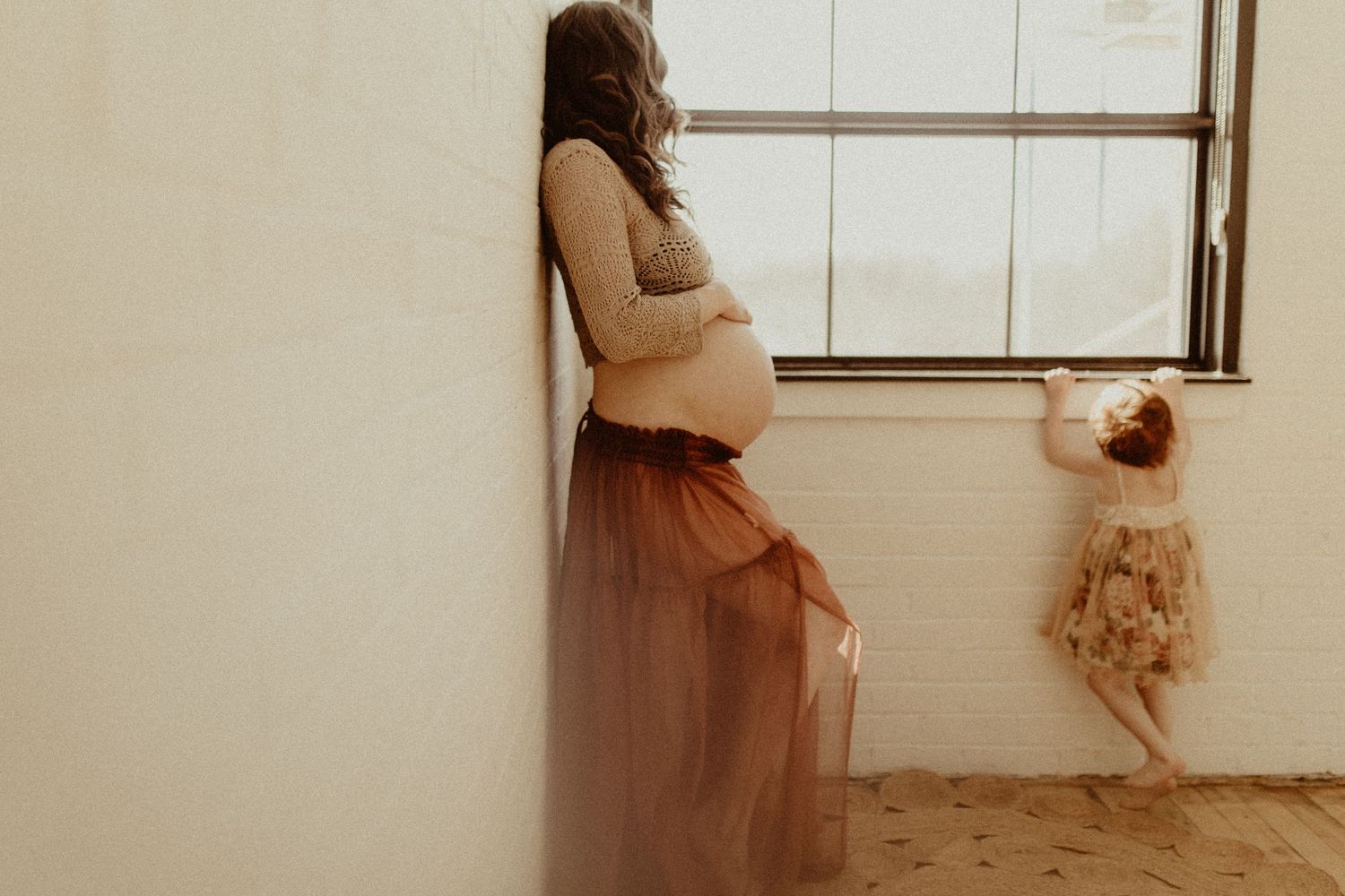 Mom holding her baby bump as she watches her daughter in soft light by artistic Bowmanville, ON family photographer.